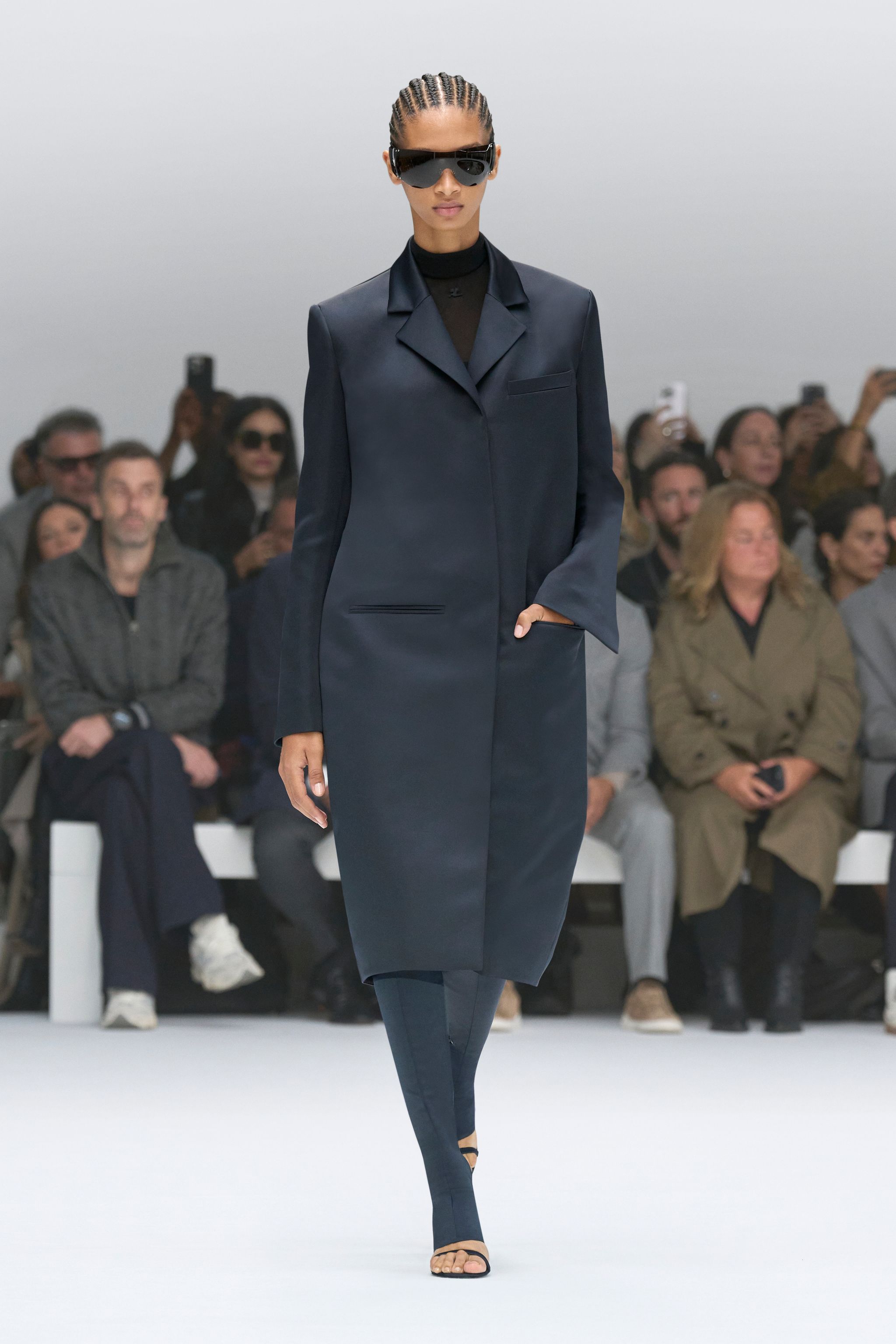 Elegant navy coat by Courrèges showcased on runway with confident model and audience.