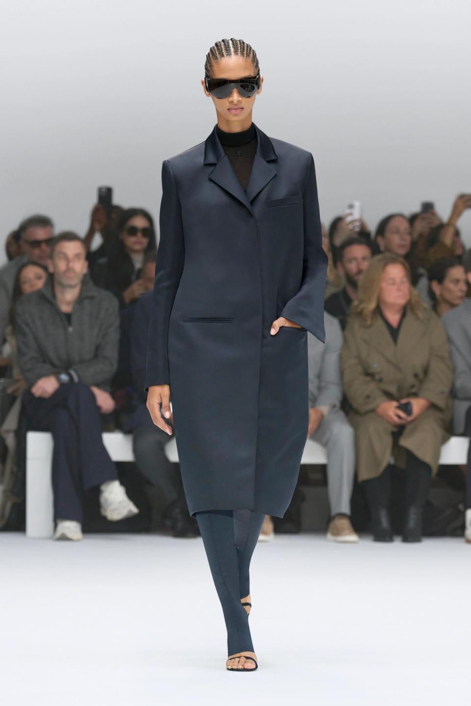 Elegant navy coat by Courrèges showcased on runway with confident model and audience.