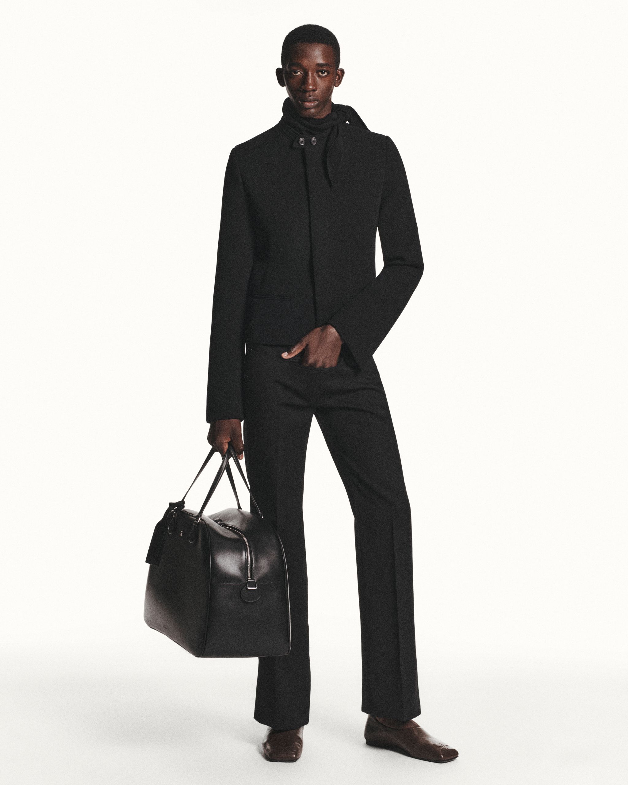 Elegant black tailored jacket and trousers with a sleek designer bag by Courrèges.