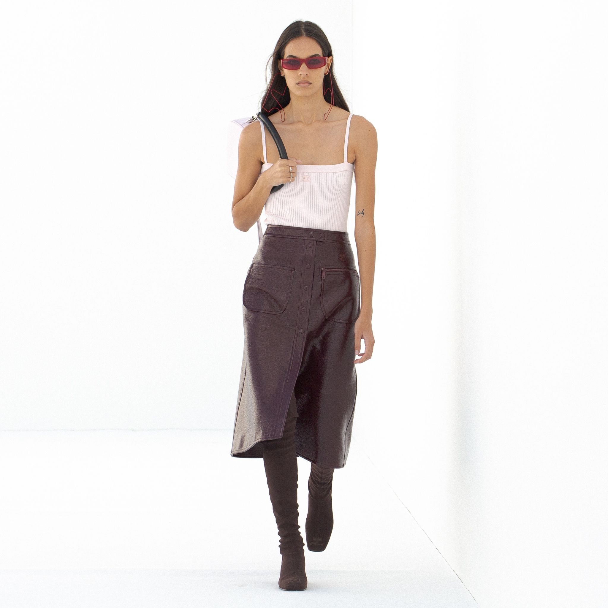 Elegant female model wearing Courrèges fashion, leather skirt, stylish sunglasses, and accessories.