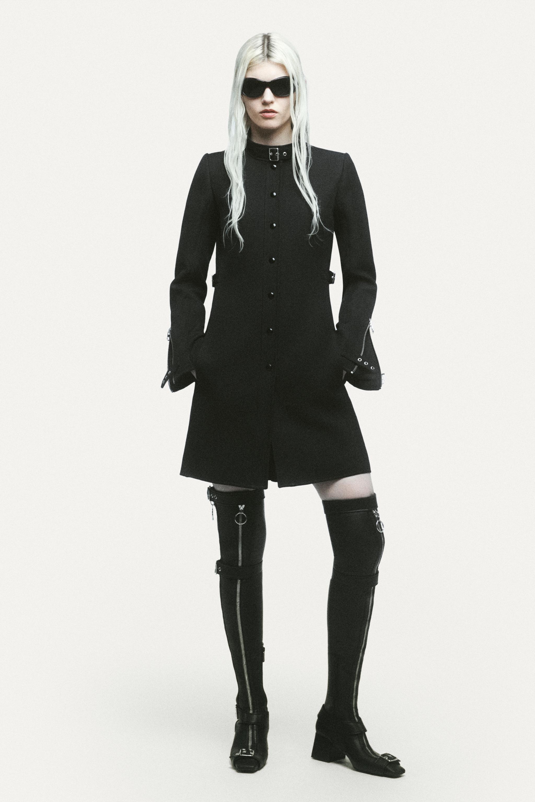 Elegant black dress with zipper details, oversized sunglasses, and knee-high boots, Courrèges fashion.