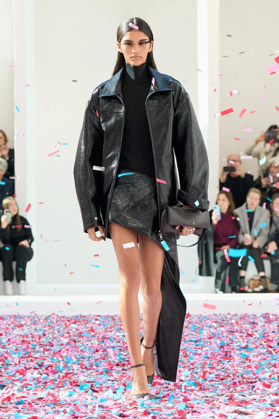 Elegant black leather jacket and skirt by Courrèges showcased on the runway with confetti.