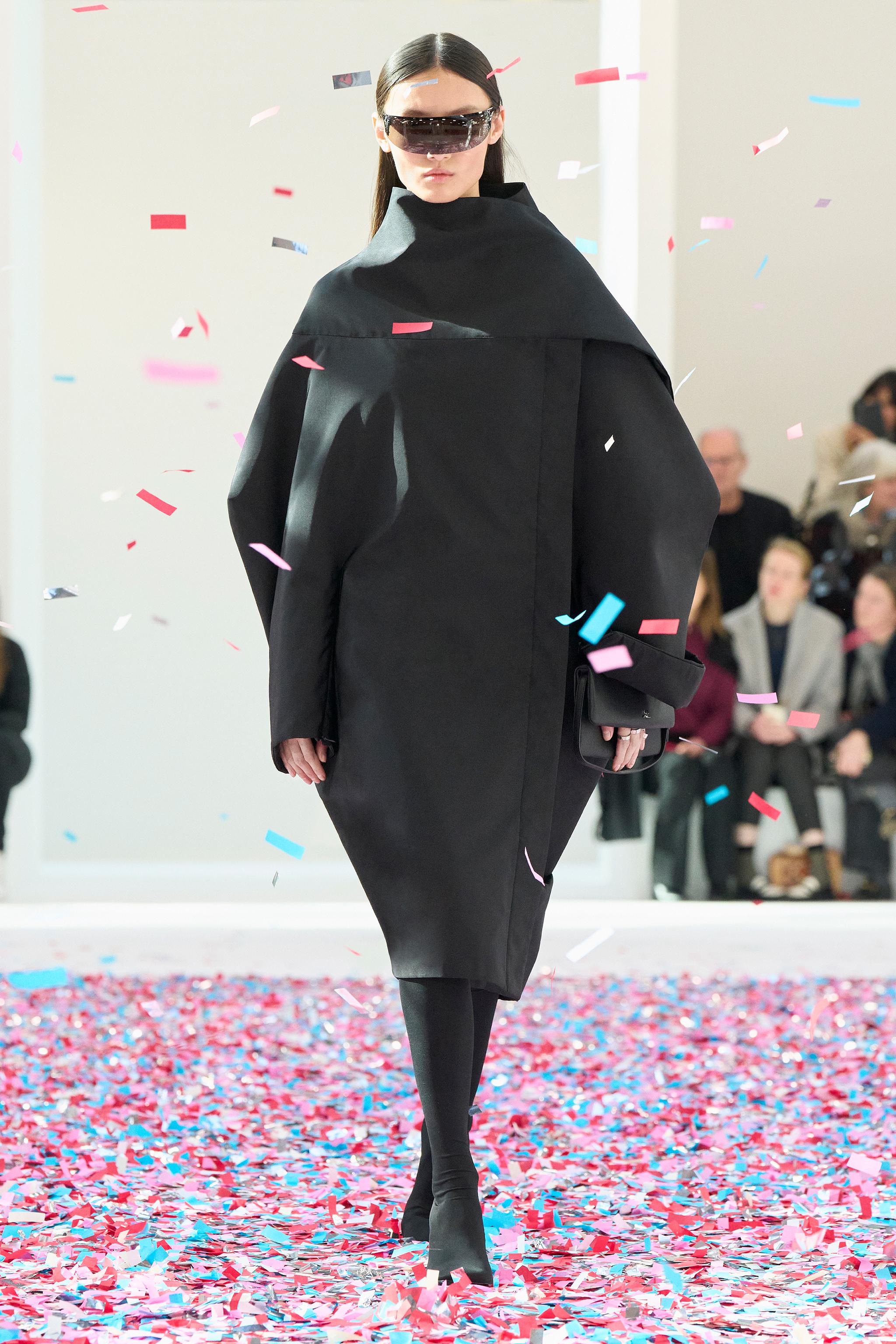 Elegant fashion model showcasing Courrèges avant-garde black coat with sunglasses on a runway.
