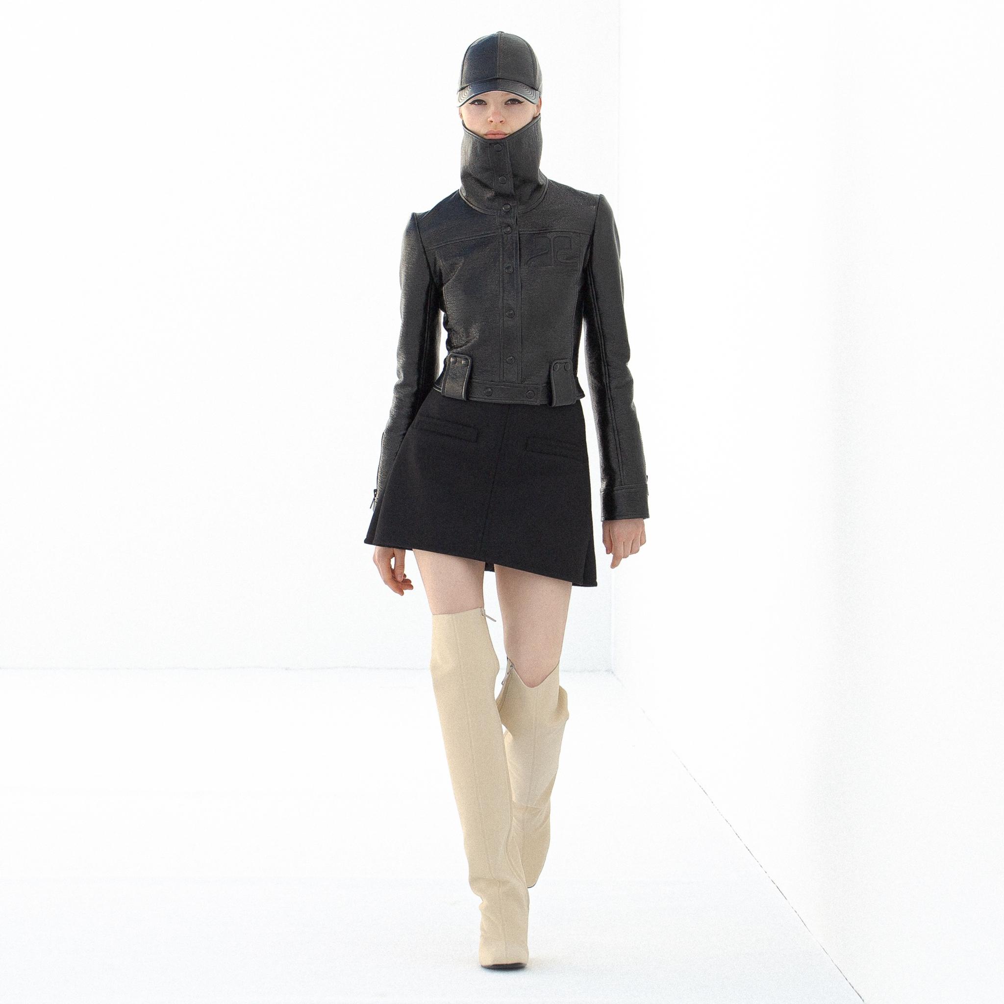 Veston en cuir noir élégant et bottes hautes blanches cassées, présenté sur un podium pour Courrèges.