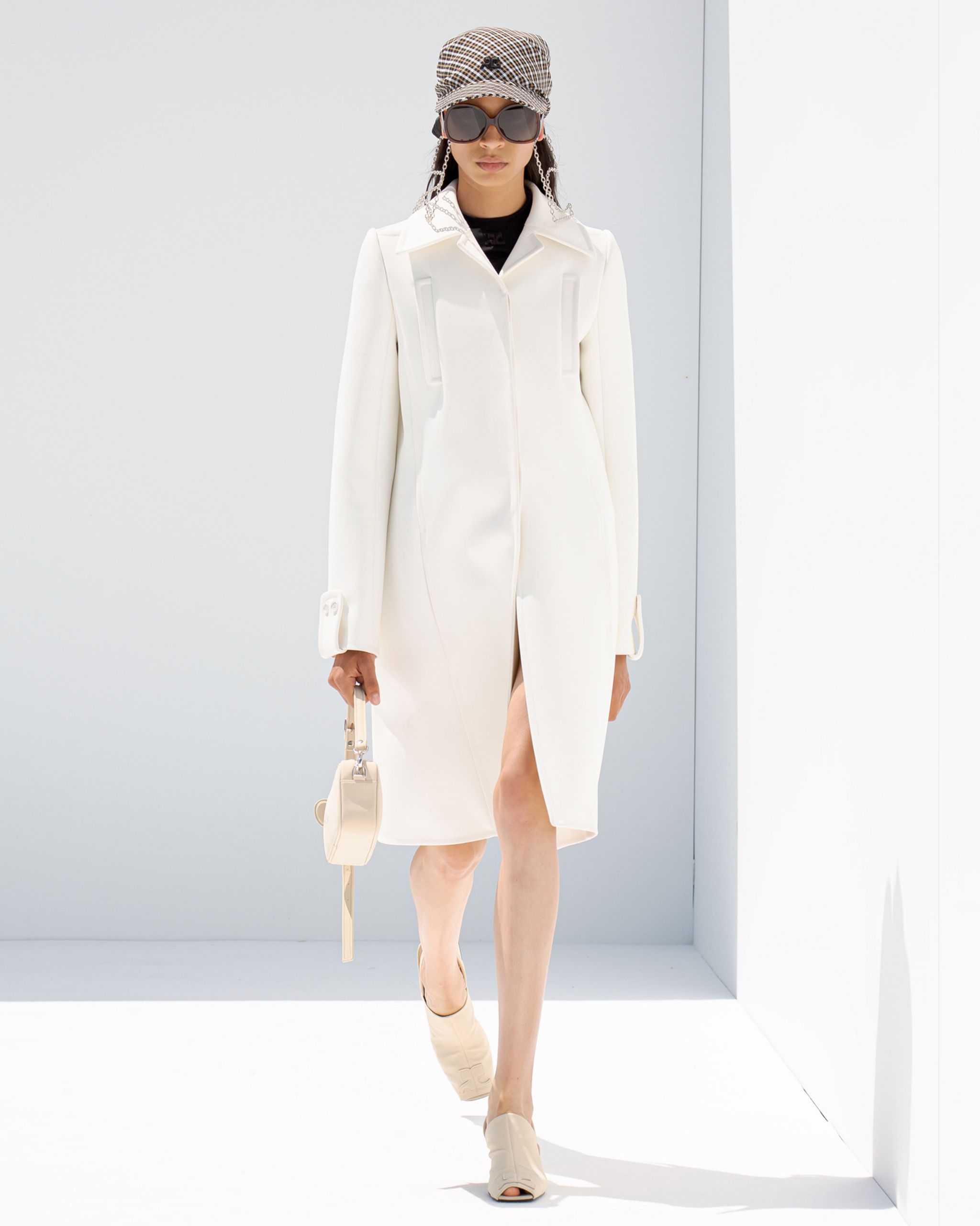 Elegant white dress with modern design by Courrèges, styled with accessories on a runway.