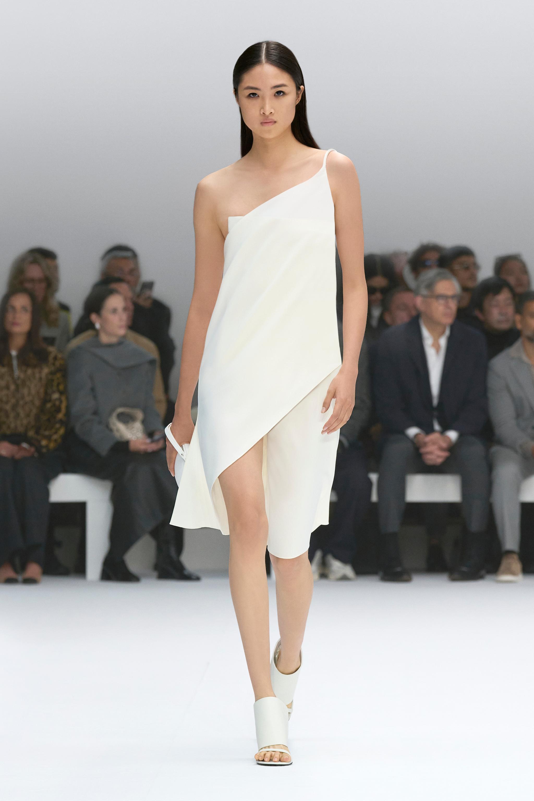 Elegant white asymmetrical dress by Courrèges showcased on a runway for a fashion brand display.