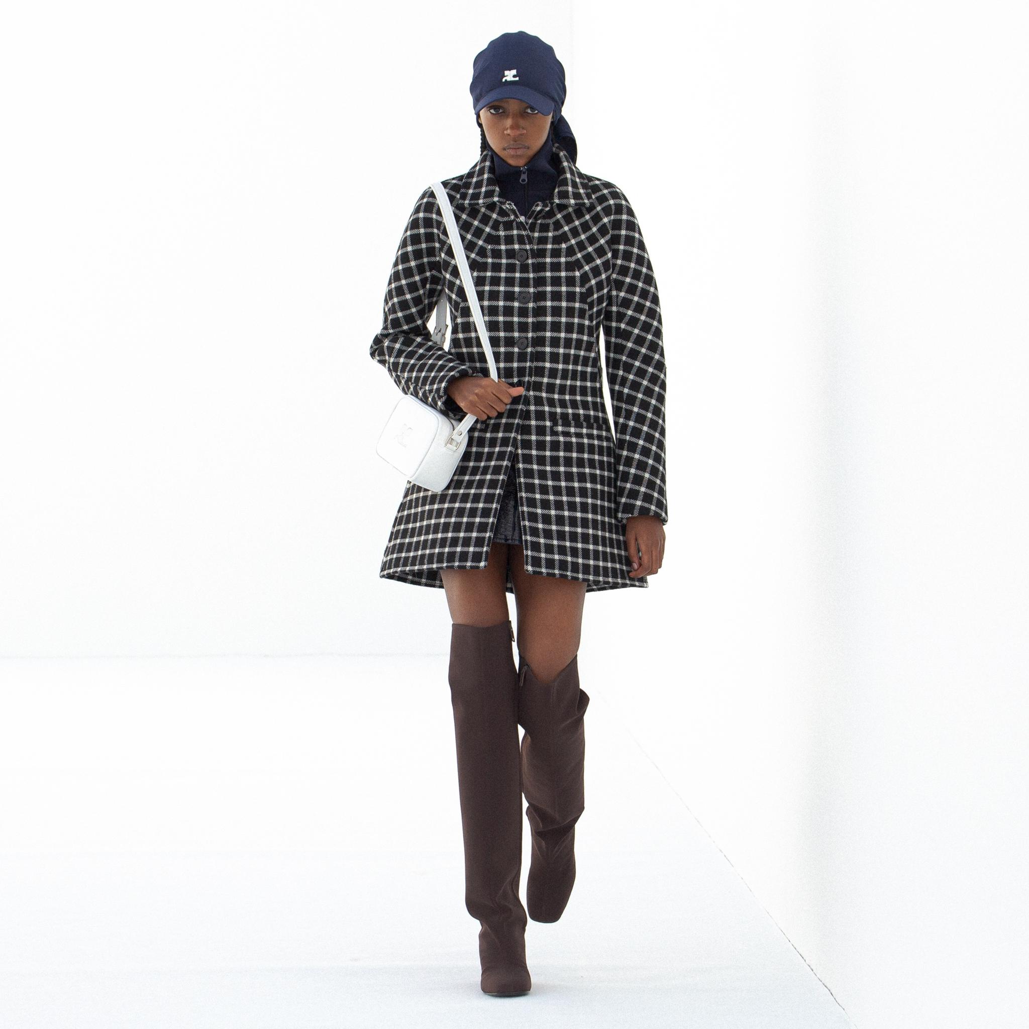 Modèle portant un manteau à carreaux Courrèges et des bottes au genou pour un style chic.