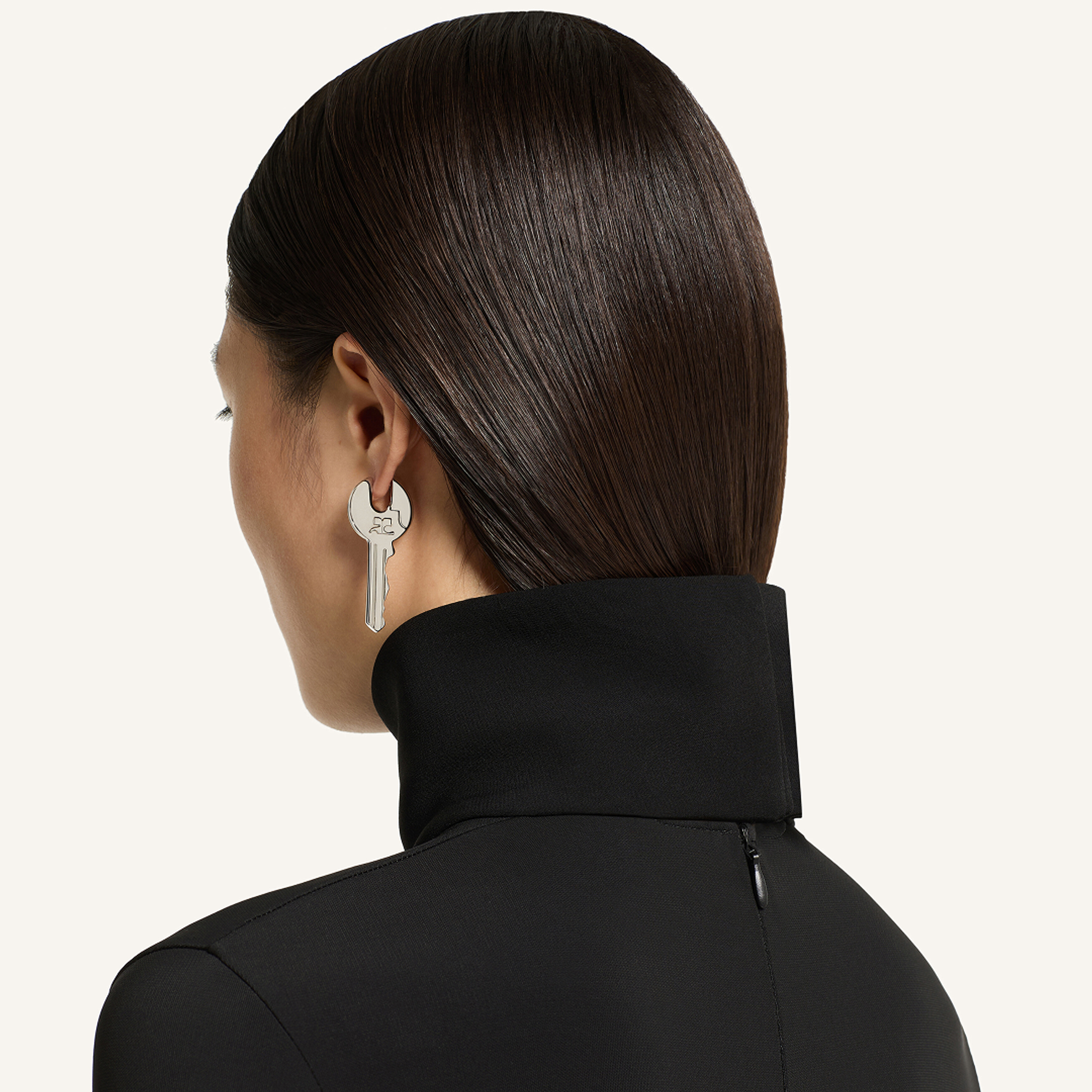Femme élégante avec des cheveux bruns lisses et un col roulé noir, portant une boucles d'oreille en forme d'étoile, évoquant Courrèges.