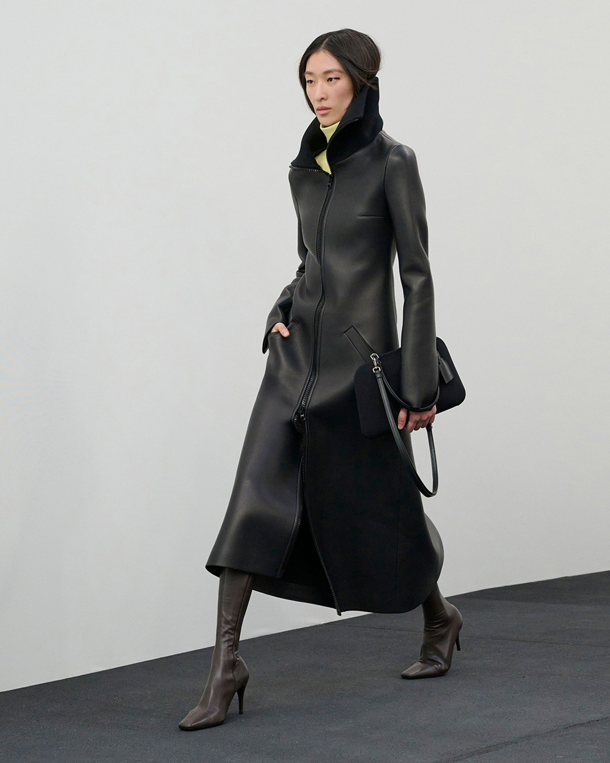 Manteau en cuir noir élégant de Courrèges, associé à des bottes hautes pour un look tendance.