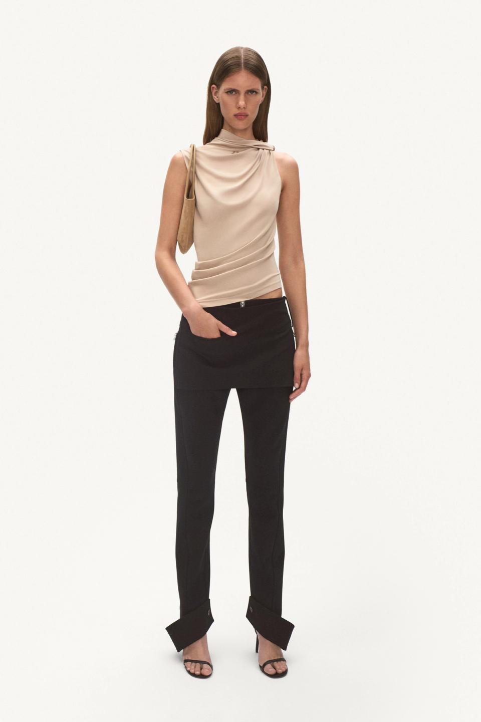 Chic model in Courrèges fashion, wearing a beige draped top and black tailored pants for women.