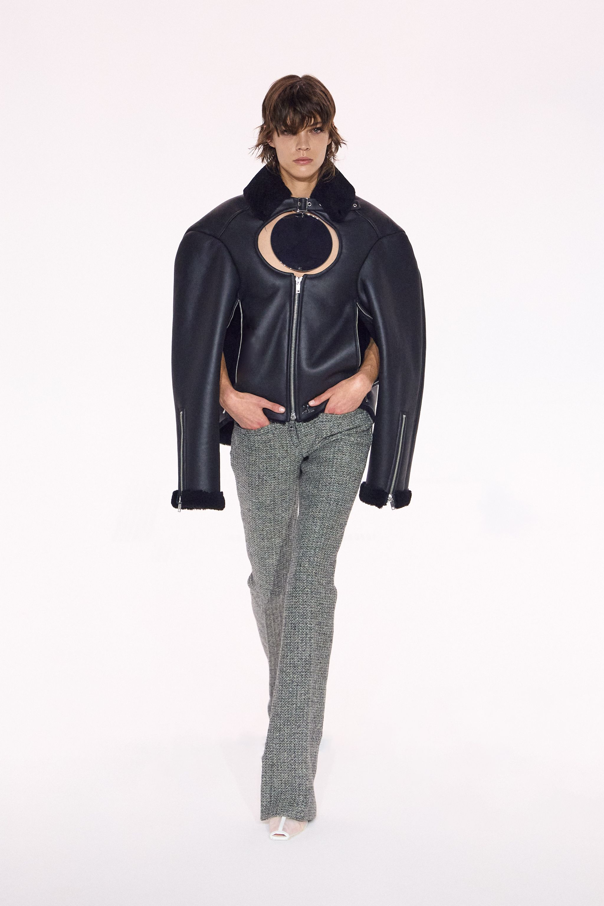 Elegant model wearing a black leather jacket with unique circular cutout, part of Courrèges collection.