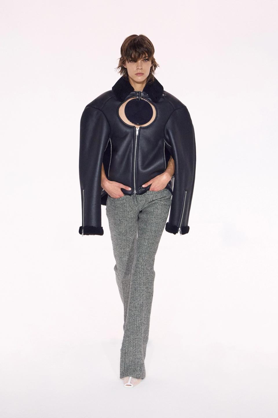 Elegant model wearing a black leather jacket with unique circular cutout, part of Courrèges collection.