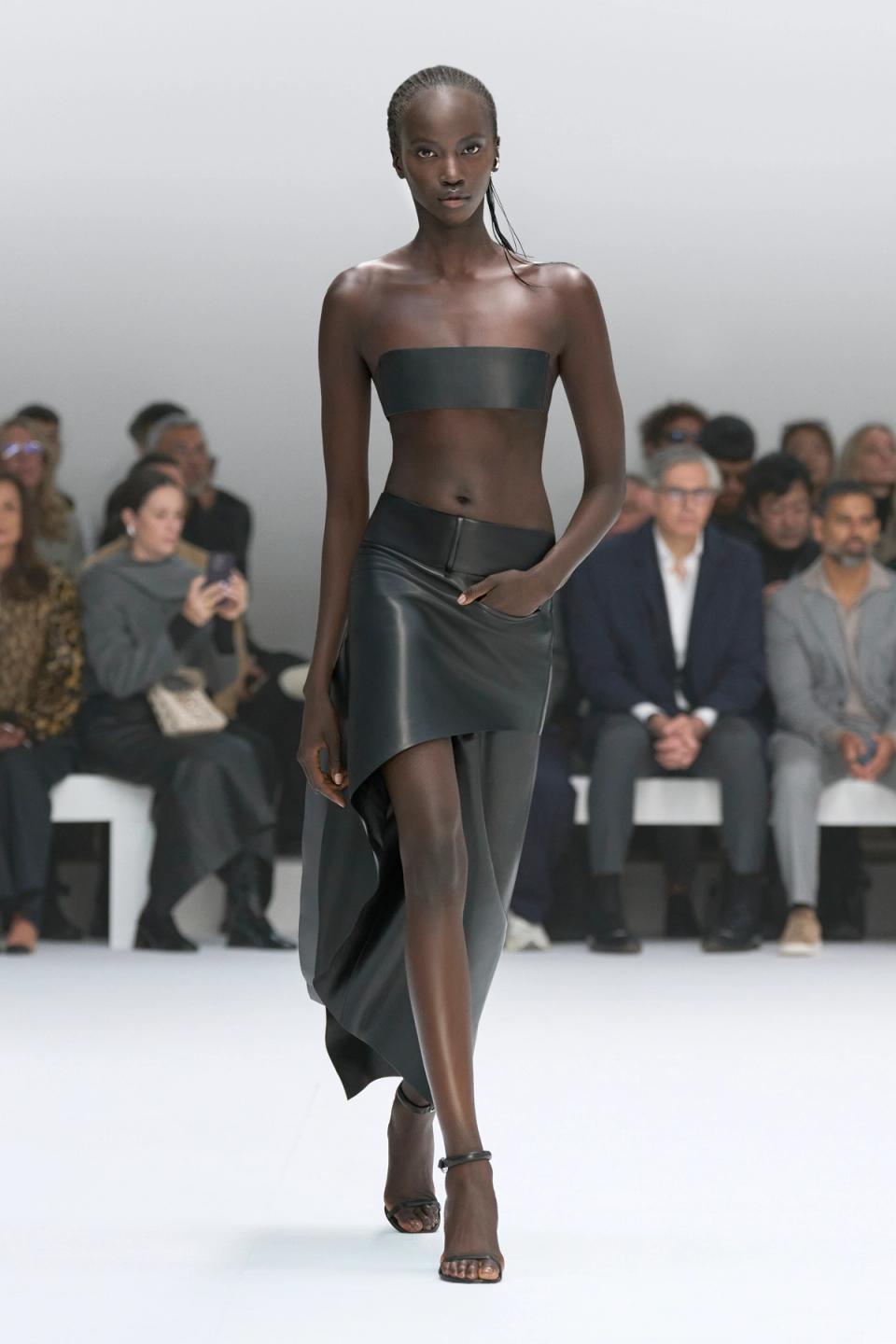 Elegant black leather midriff top and asymmetric skirt showcased on a runway for Courrèges.