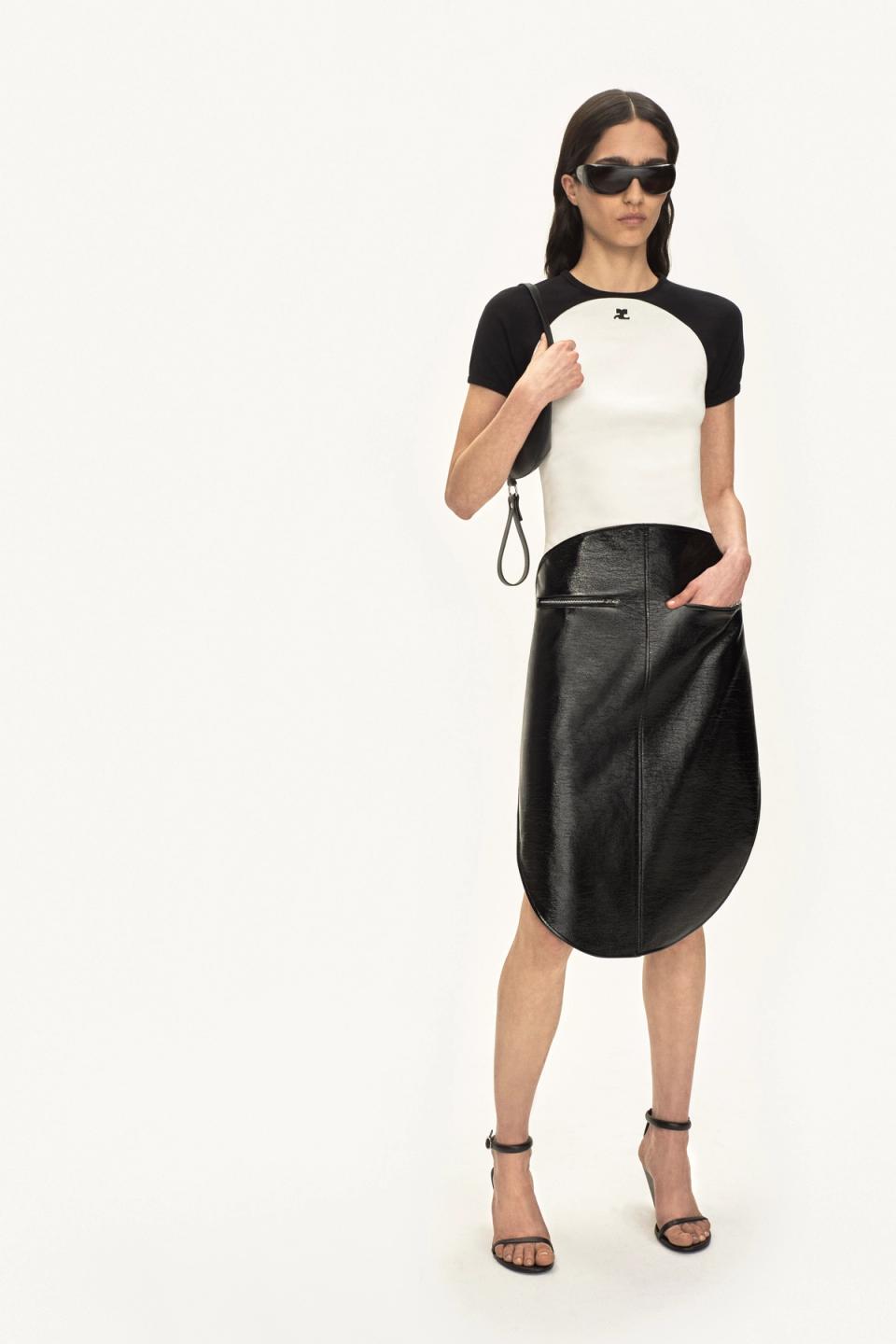Fashion model wearing black sunglasses, white and black top, and a large black leather skirt on an ecommerce site for Courrèges.