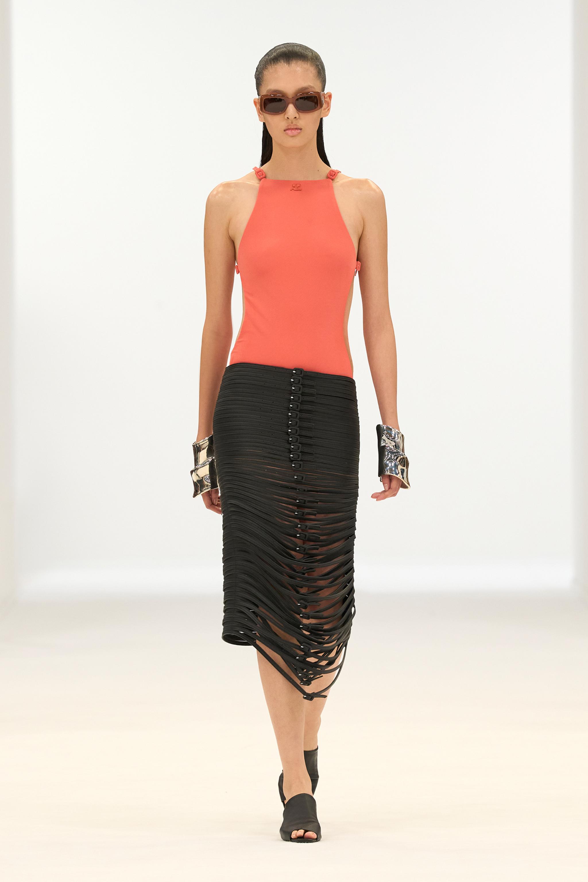 Elegant model wearing a coral tank top and black cut-out skirt for Courrèges fashion.