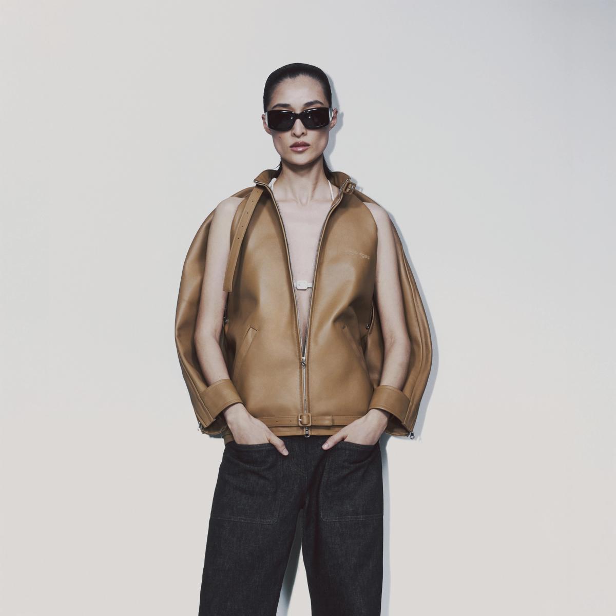 Elegant model in Courrèges fashion wearing a tan leather vest and stylish black sunglasses.