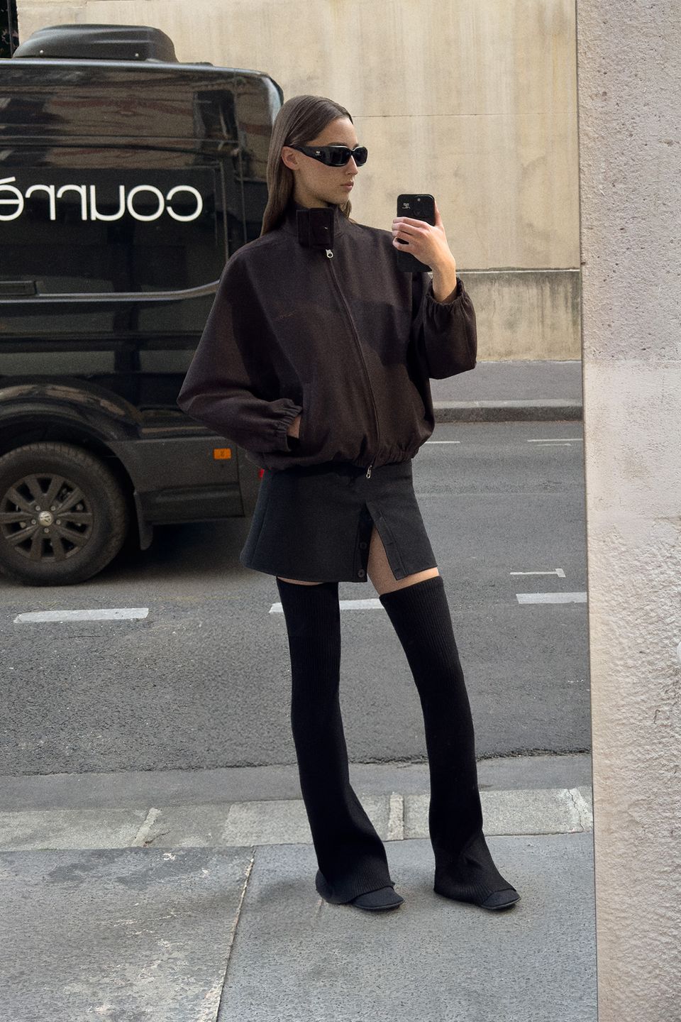 Stylish woman in Courrèges fashion, wearing dark oversized jacket, miniskirt, and sunglasses.