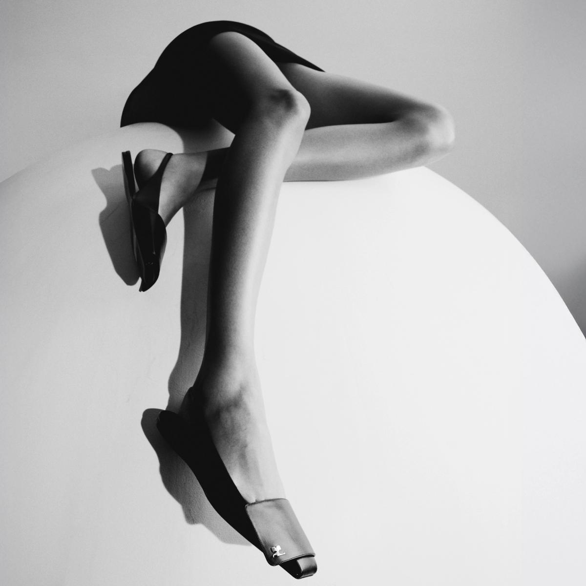 Chaussures à talons noirs élégantes de Courrèges sur une surface abstraite blanche stylisée.