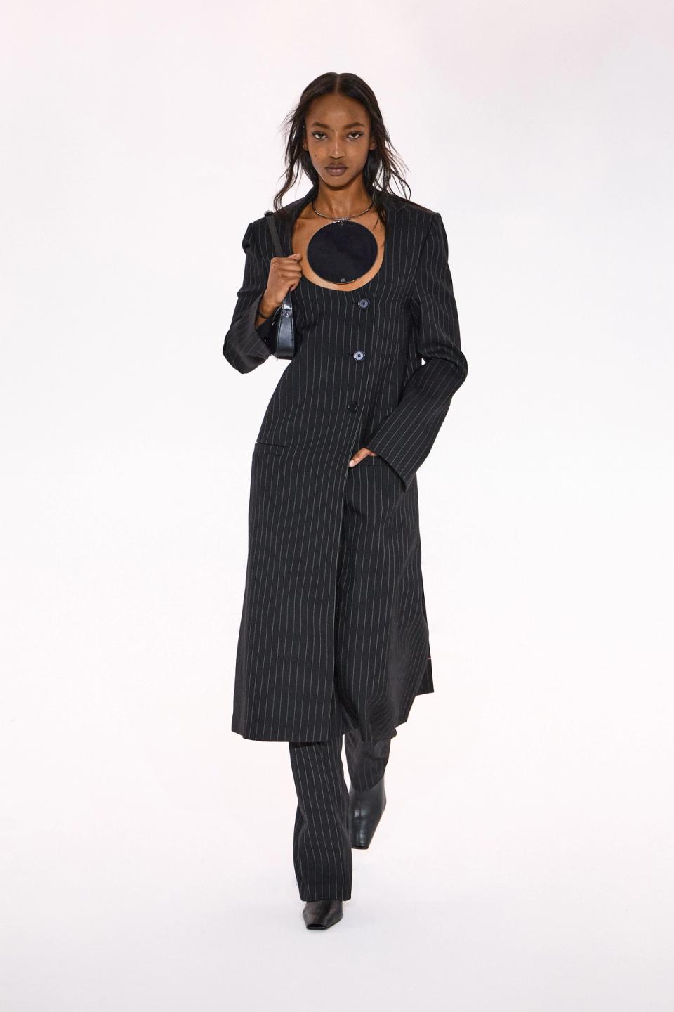 Stylish woman in pinstripe suit showcasing Courrèges fashion on an e-commerce site.