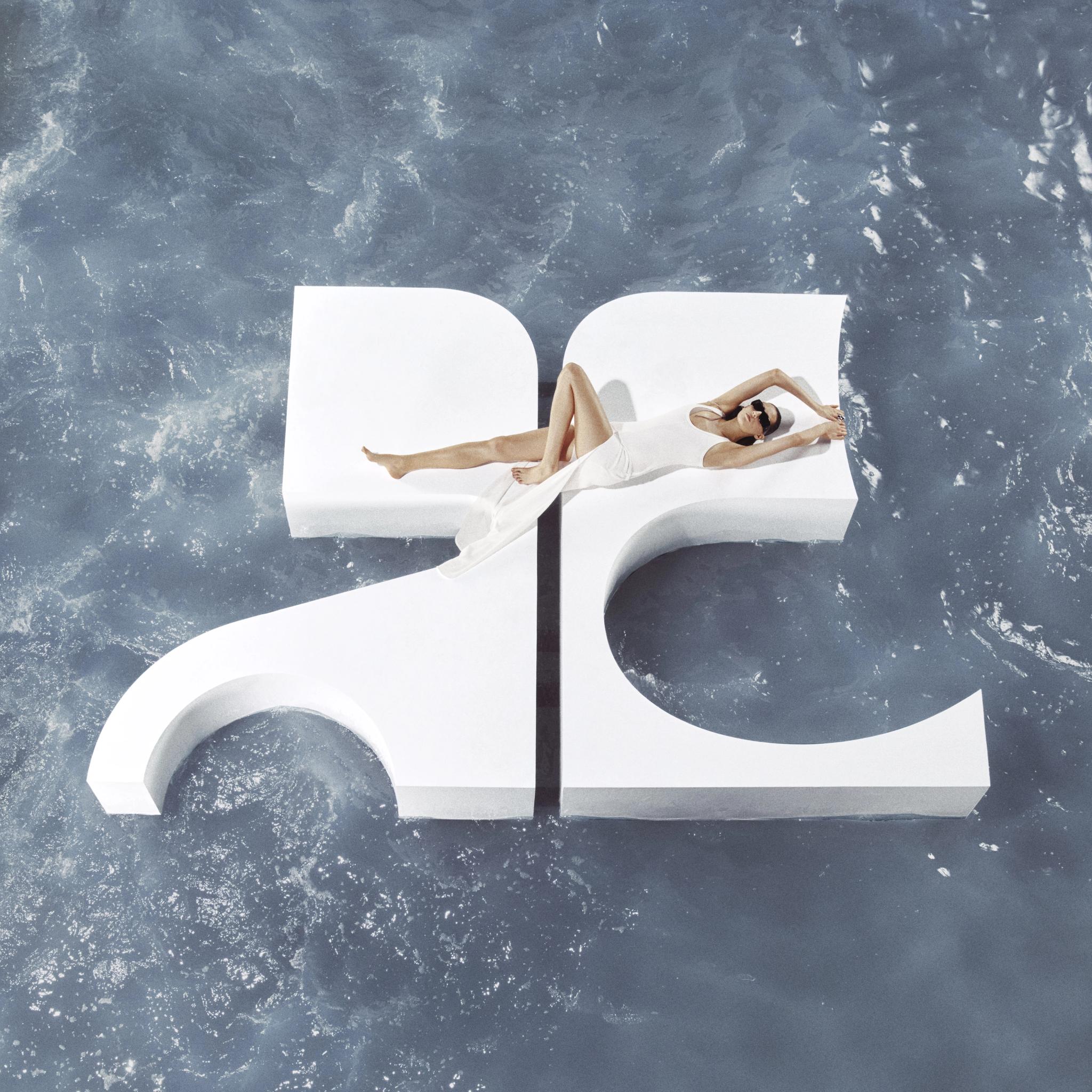 Elegant fashion model lounging on a white geometric platform over water for Courrèges.