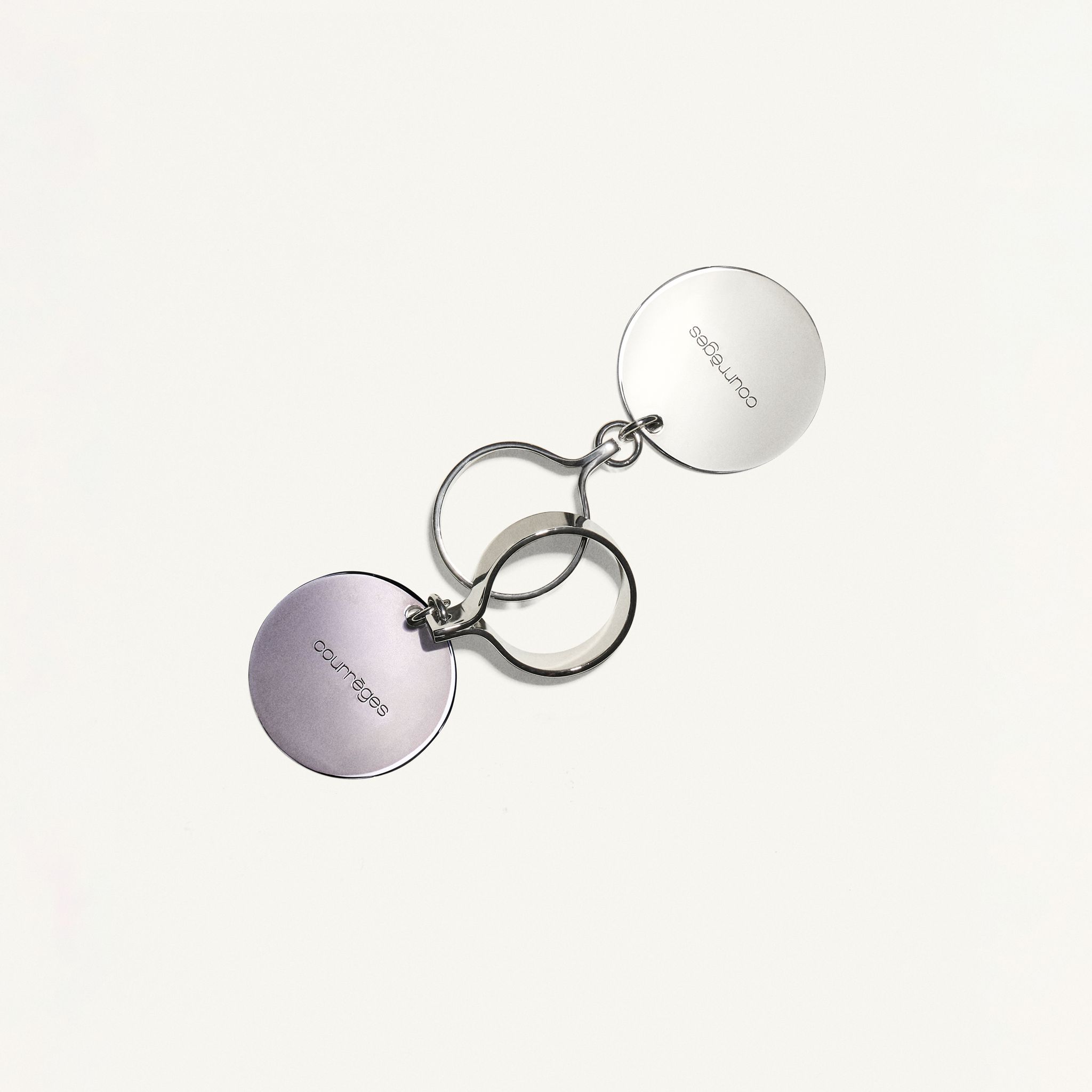 Clé magnétique élégante en argent avec plaques circulaires gravées du logo Courrèges, accessoire chic.