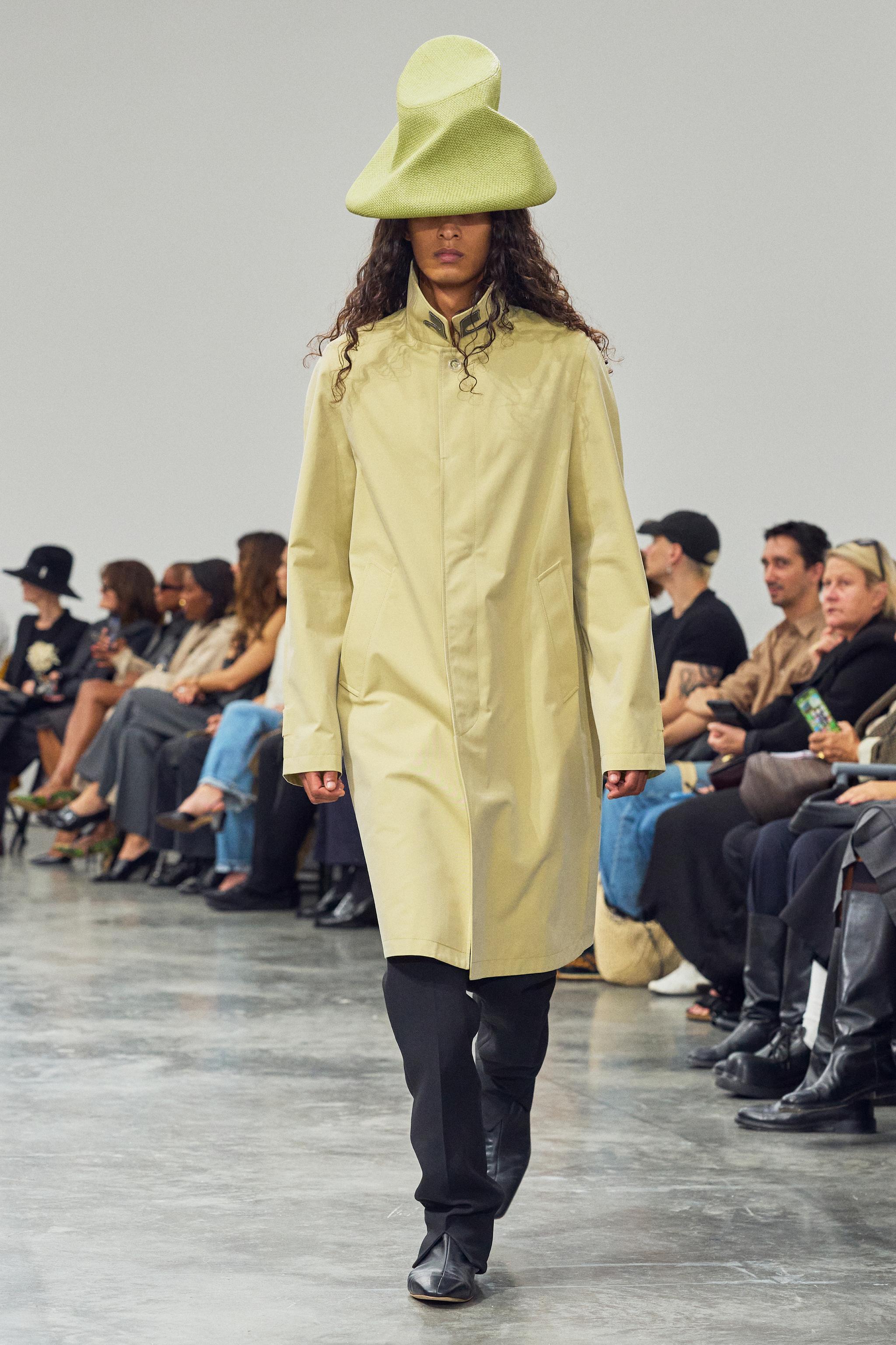 Elegant model in Courrèges fashion, walking the runway in a stylish beige coat and unique hat.