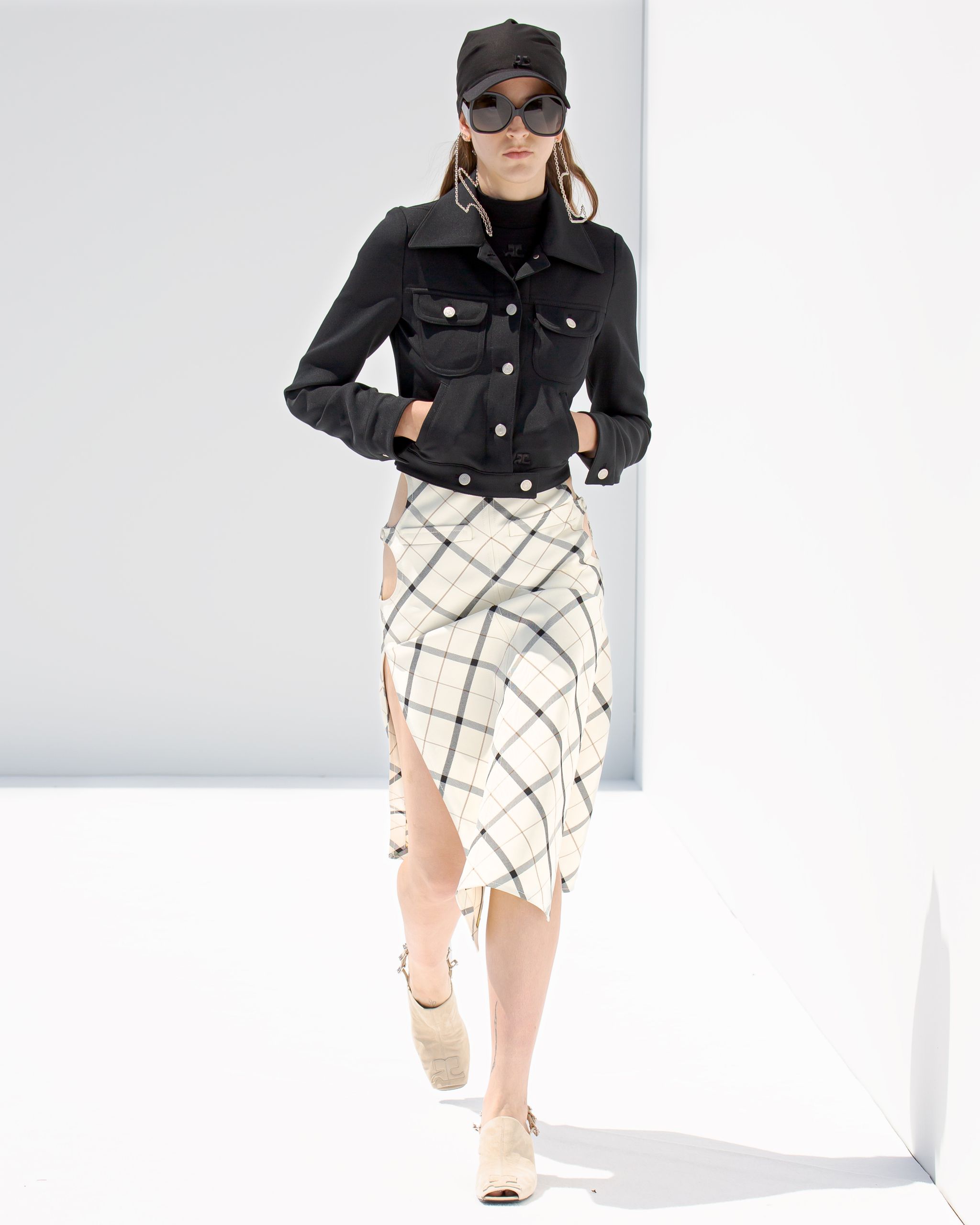 Elegant model wearing Courrèges black jacket and checkered skirt on a minimalist runway.