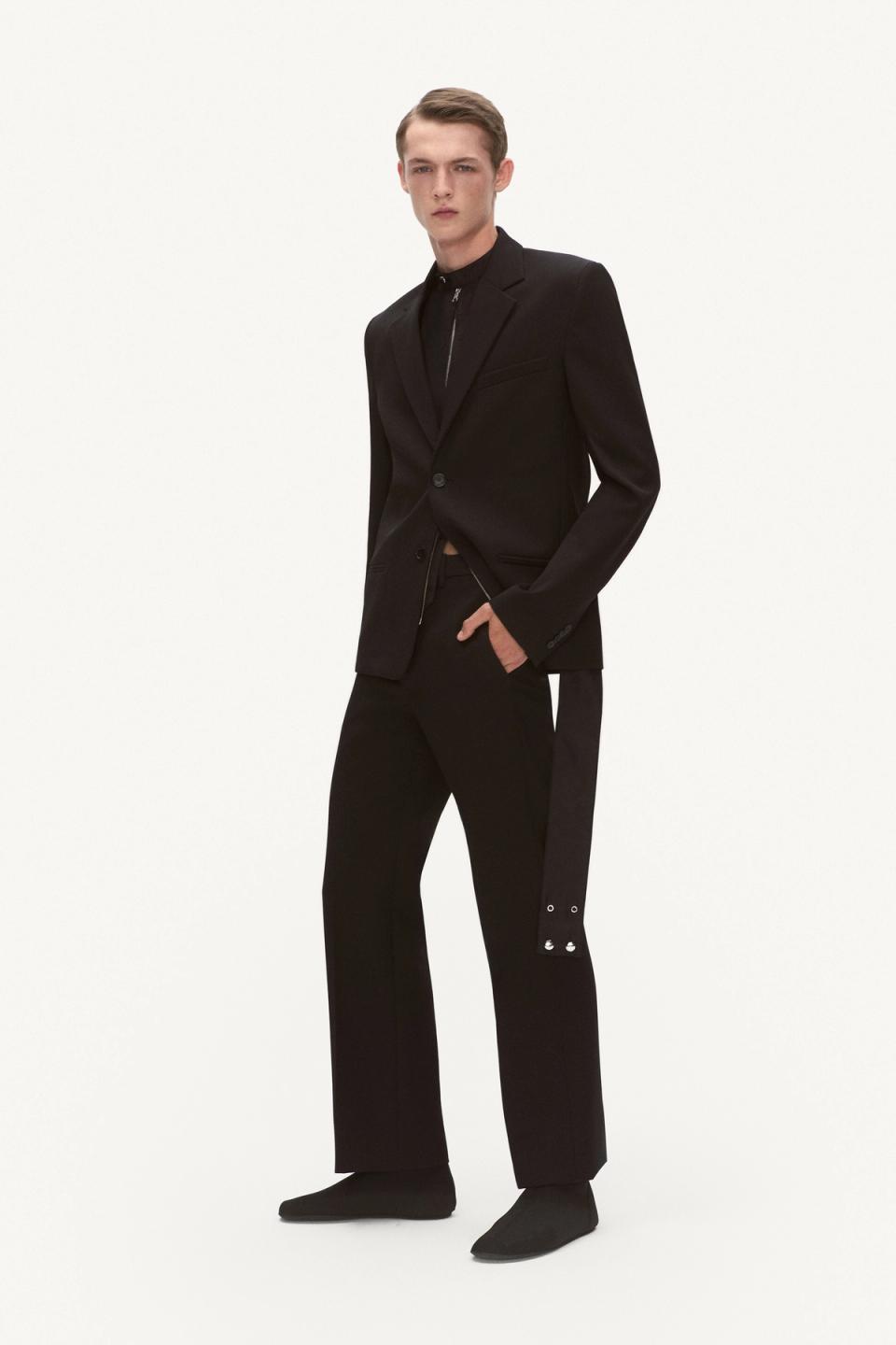 Elegant male model in black tailored Courrèges suit and footwear on a white backdrop.