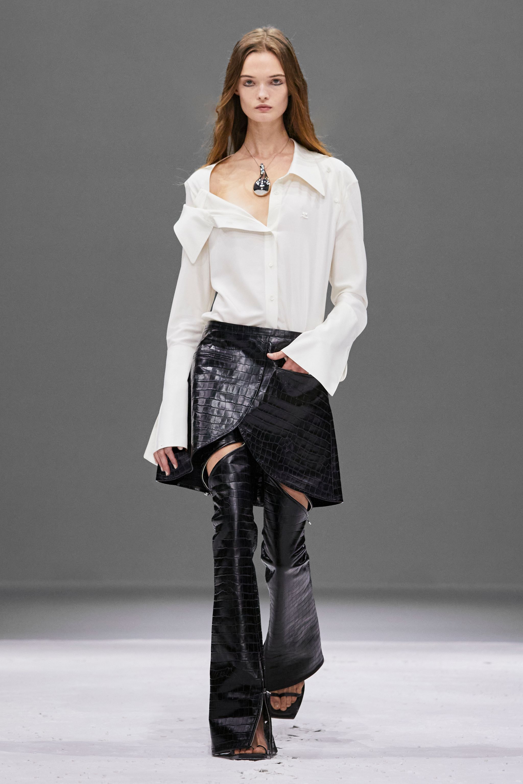 Elegant model wearing Courrèges fashion brand's sophisticated white blouse and black crocodile-effect skirt.