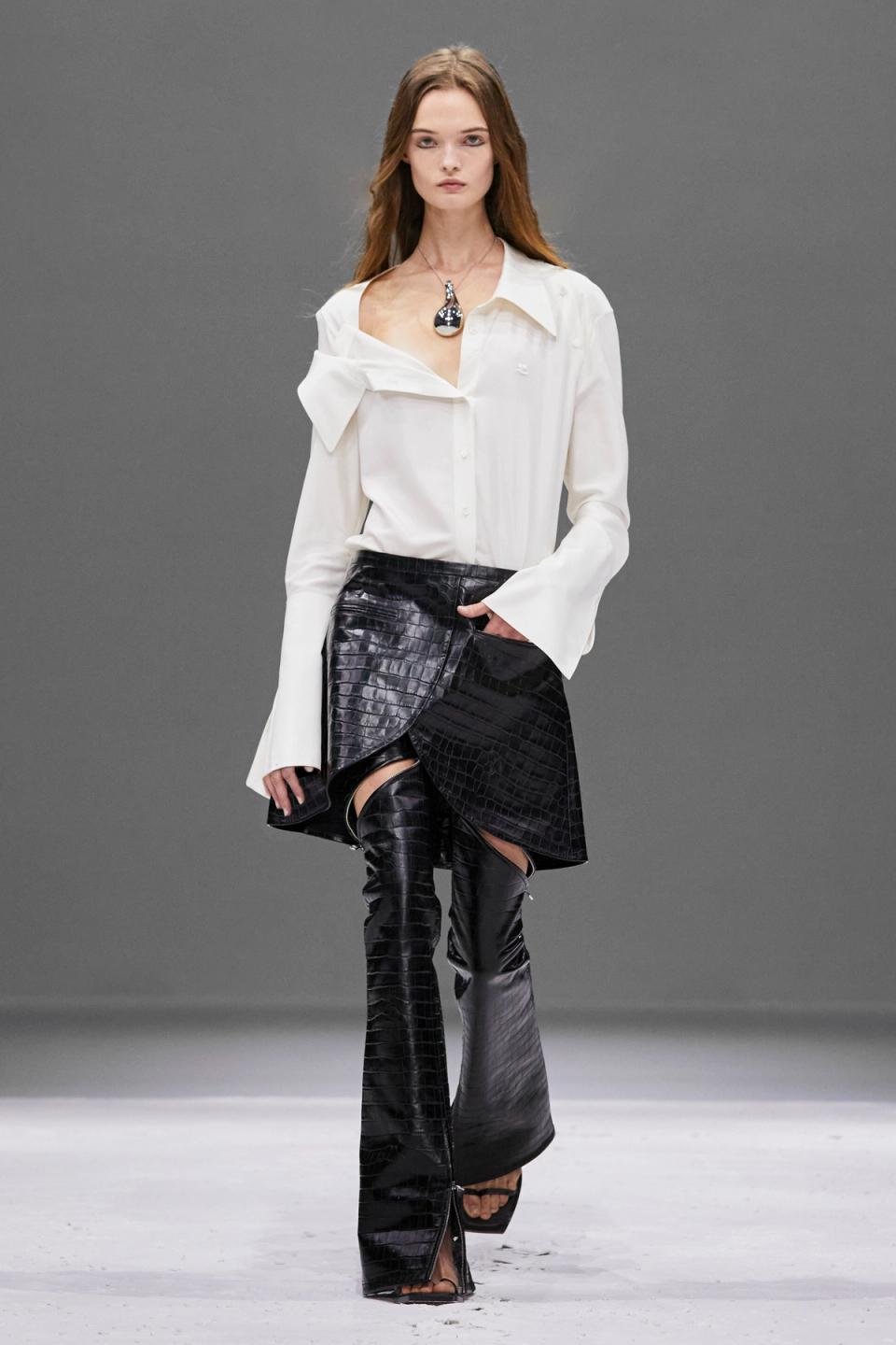 Elegant model wearing Courrèges fashion brand's sophisticated white blouse and black crocodile-effect skirt.