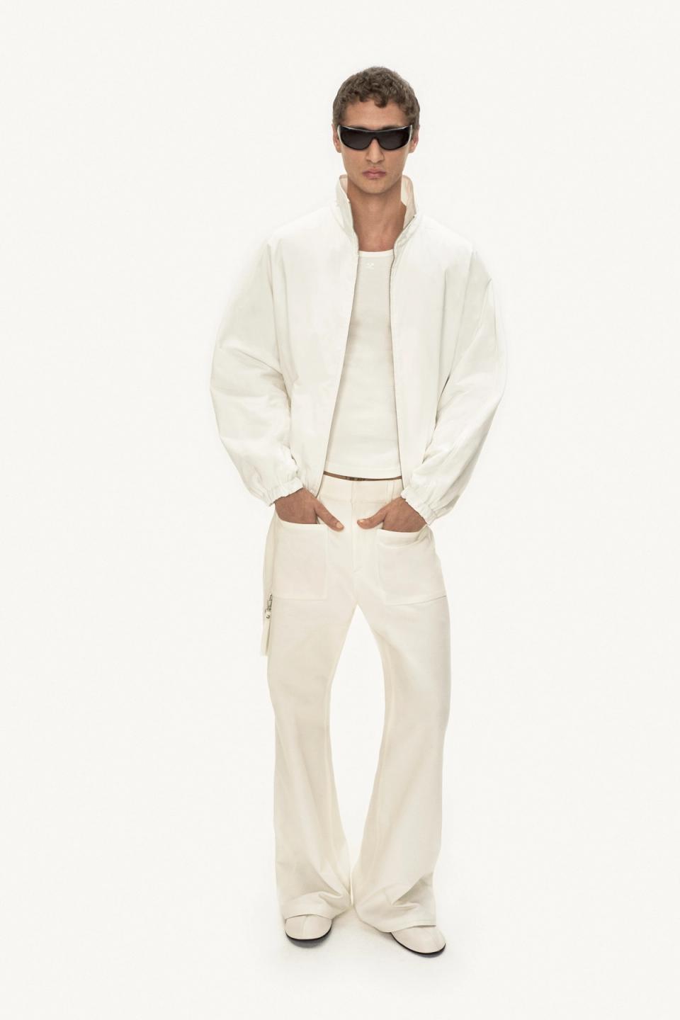Elegant male model in white Courrèges fashion, wearing stylish sunglasses on white background.