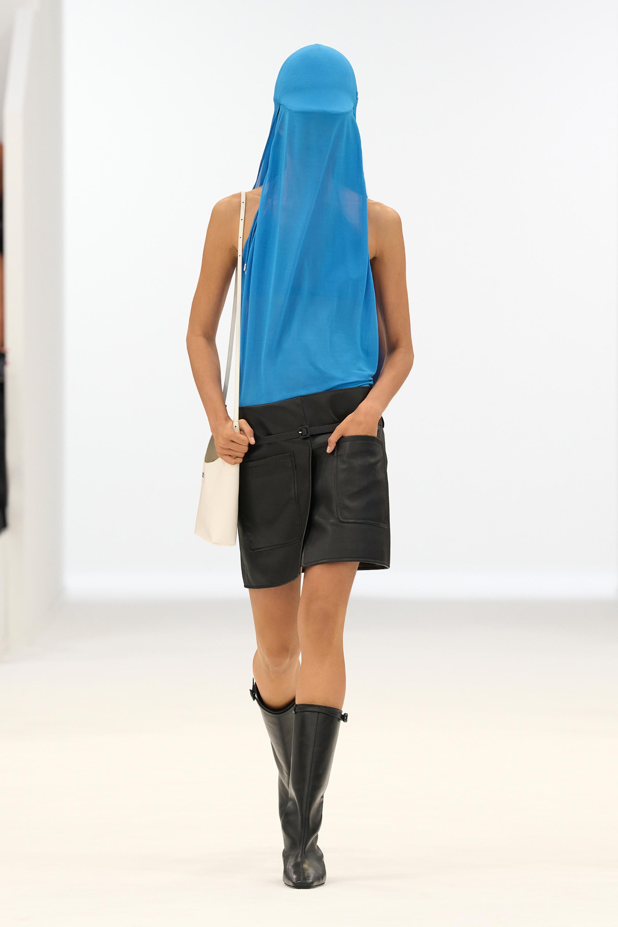Elegant Courrèges fashion with a blue sheer top, black leather skirt, and knee-high boots.