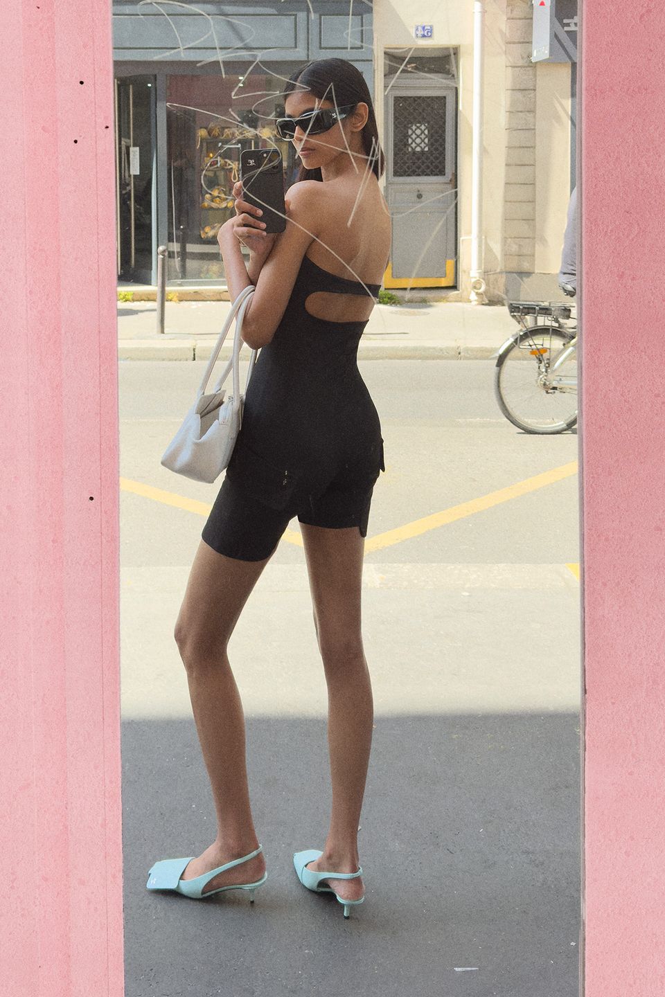Elegant woman in a black dress with cutouts, taking a selfie on a city street for Courrèges.