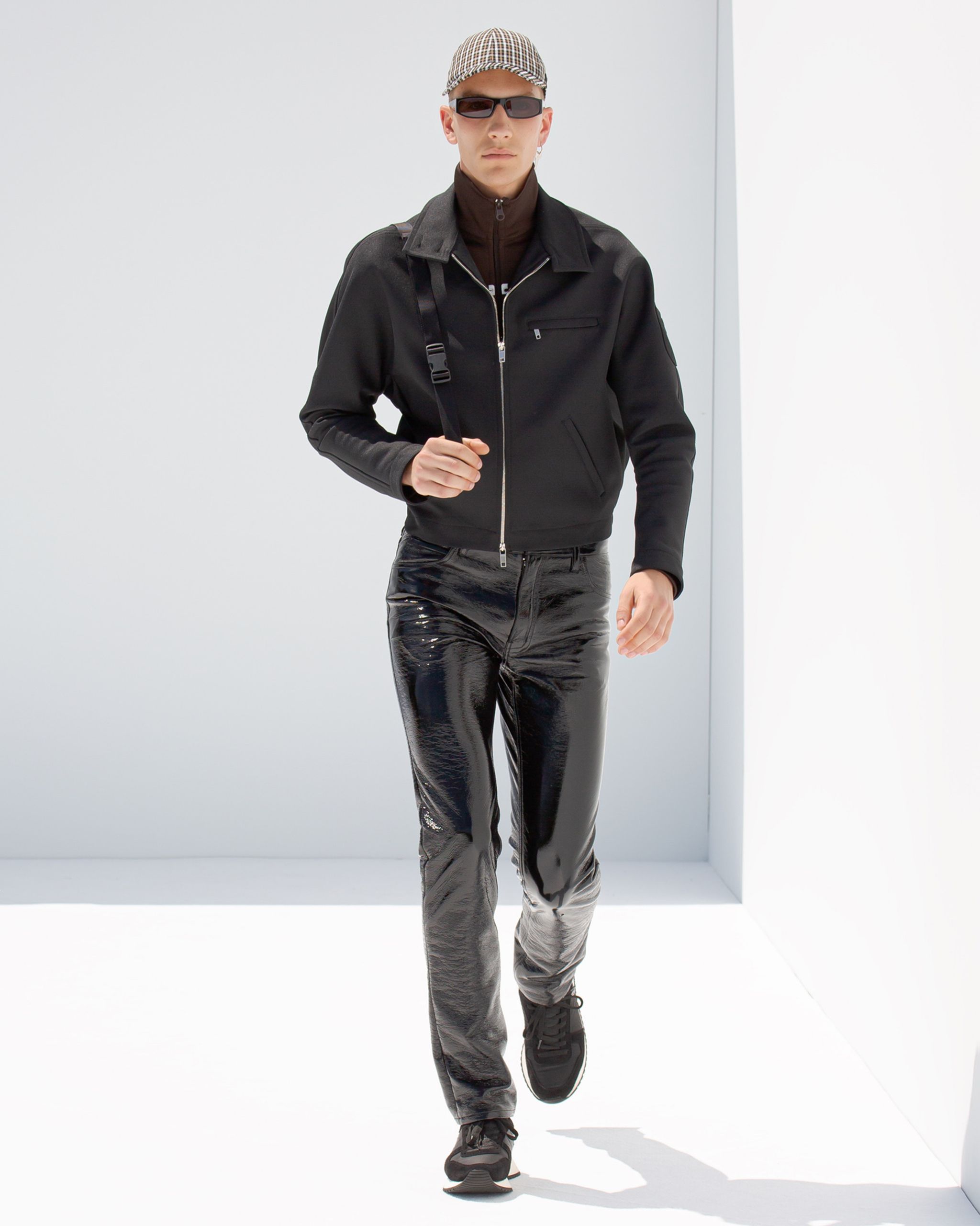 Elegant male fashion model in black Courrèges outfit on a white backdrop, showcasing modern style.