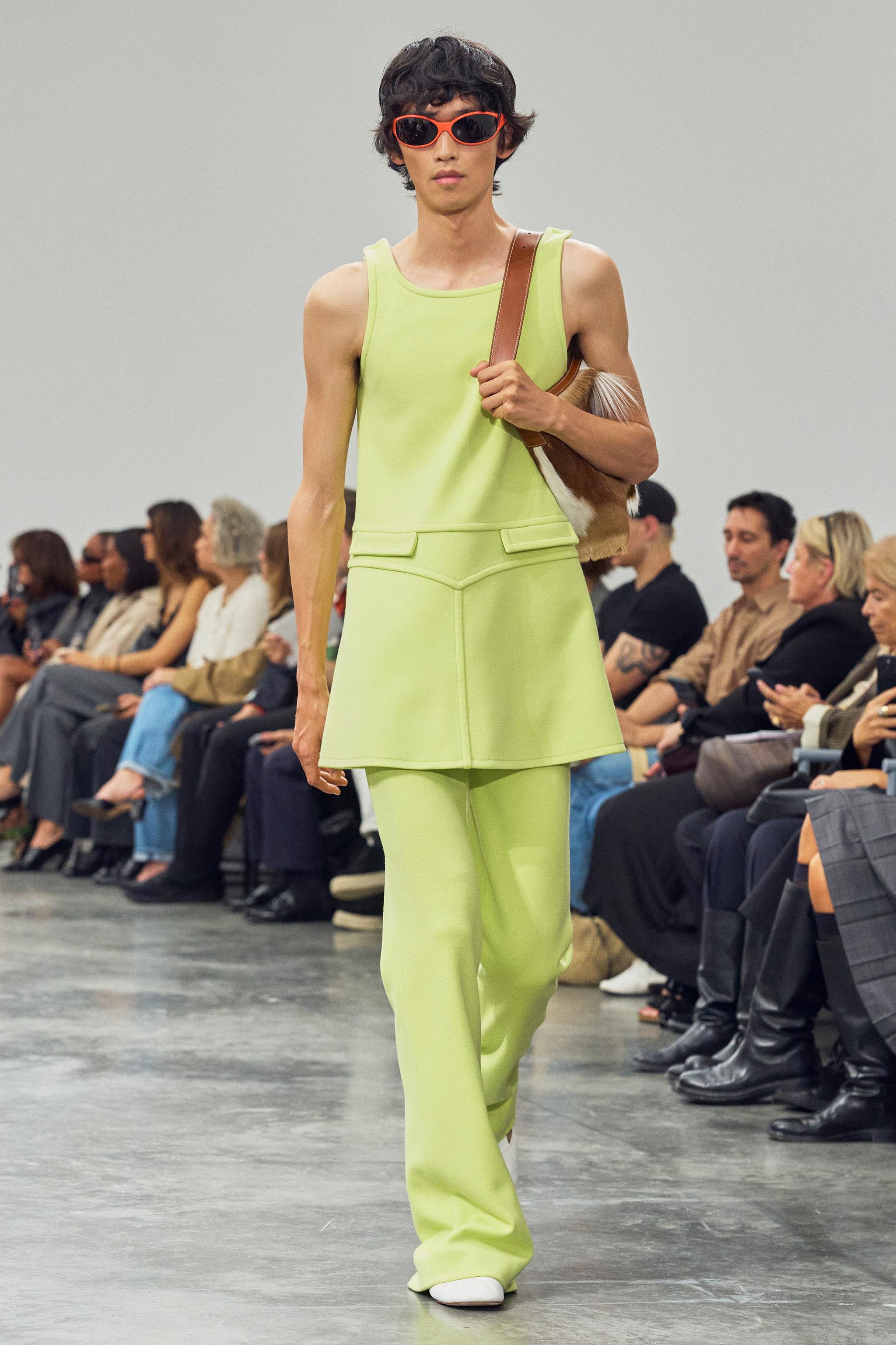 Fashion model walking runway in bold lime green suit for Courrèges collection at a runway show.