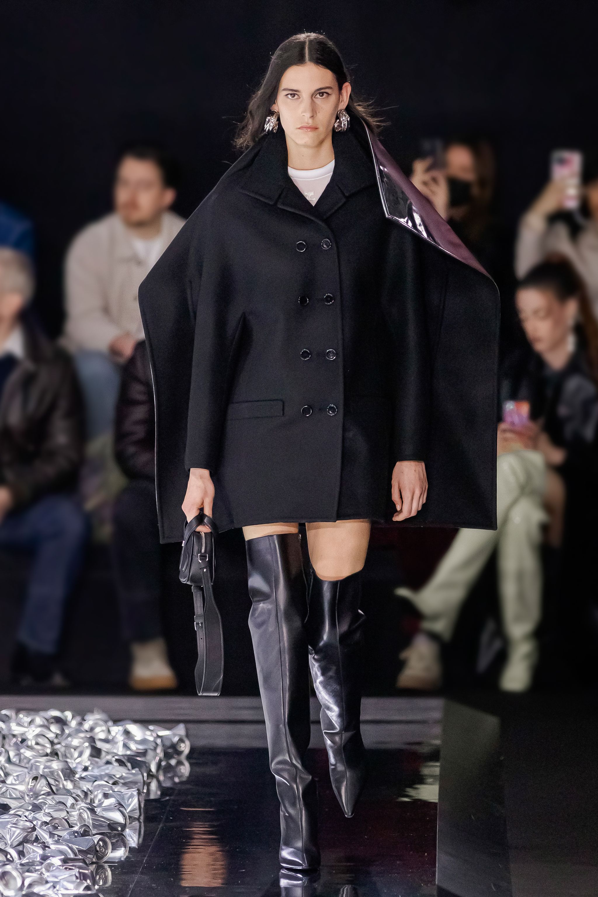 Elegant black coat with shiny accents, showcased at Courrèges fashion show for modern style.