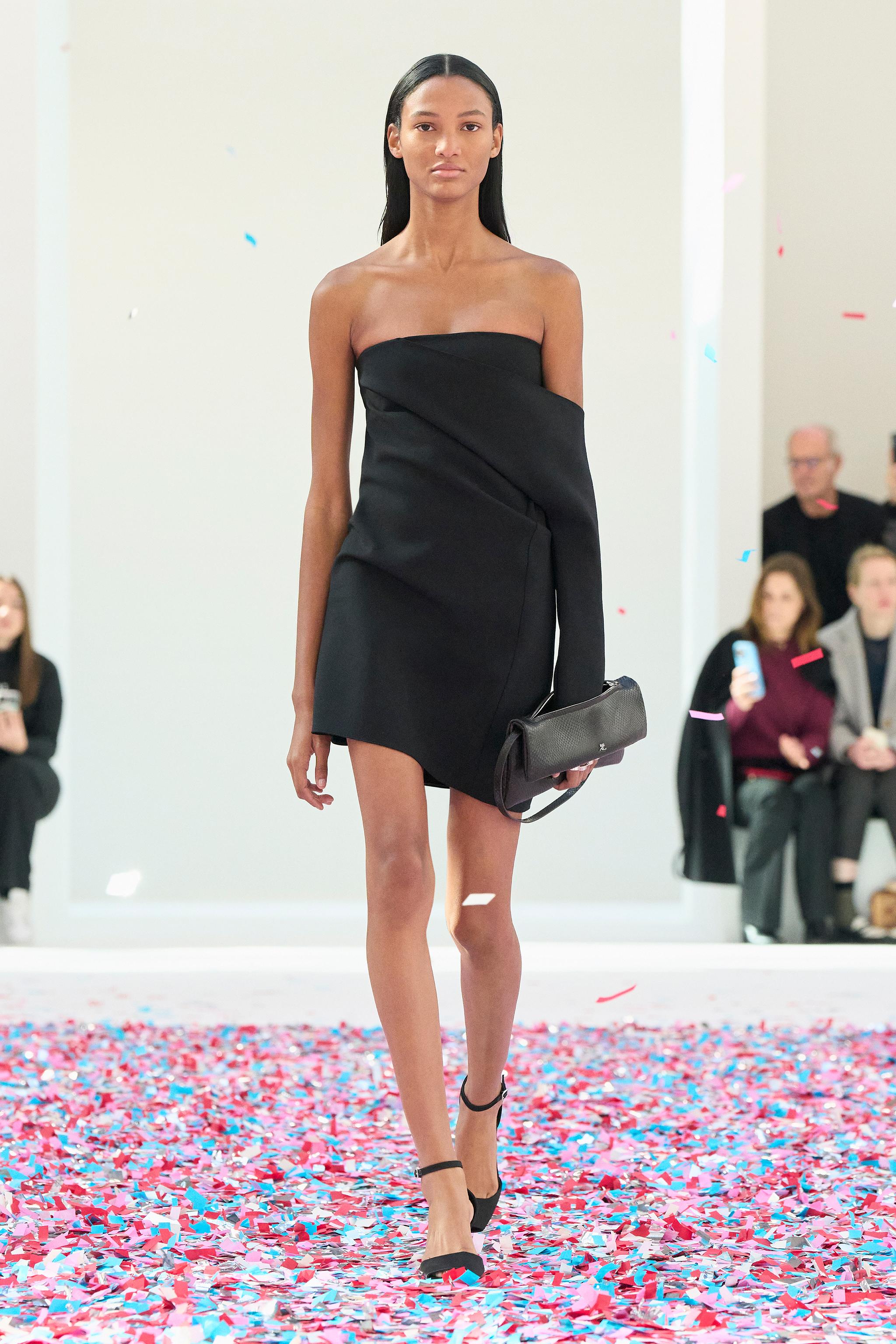 Elegant model in black Courrèges dress on runway, showcasing contemporary fashion design.