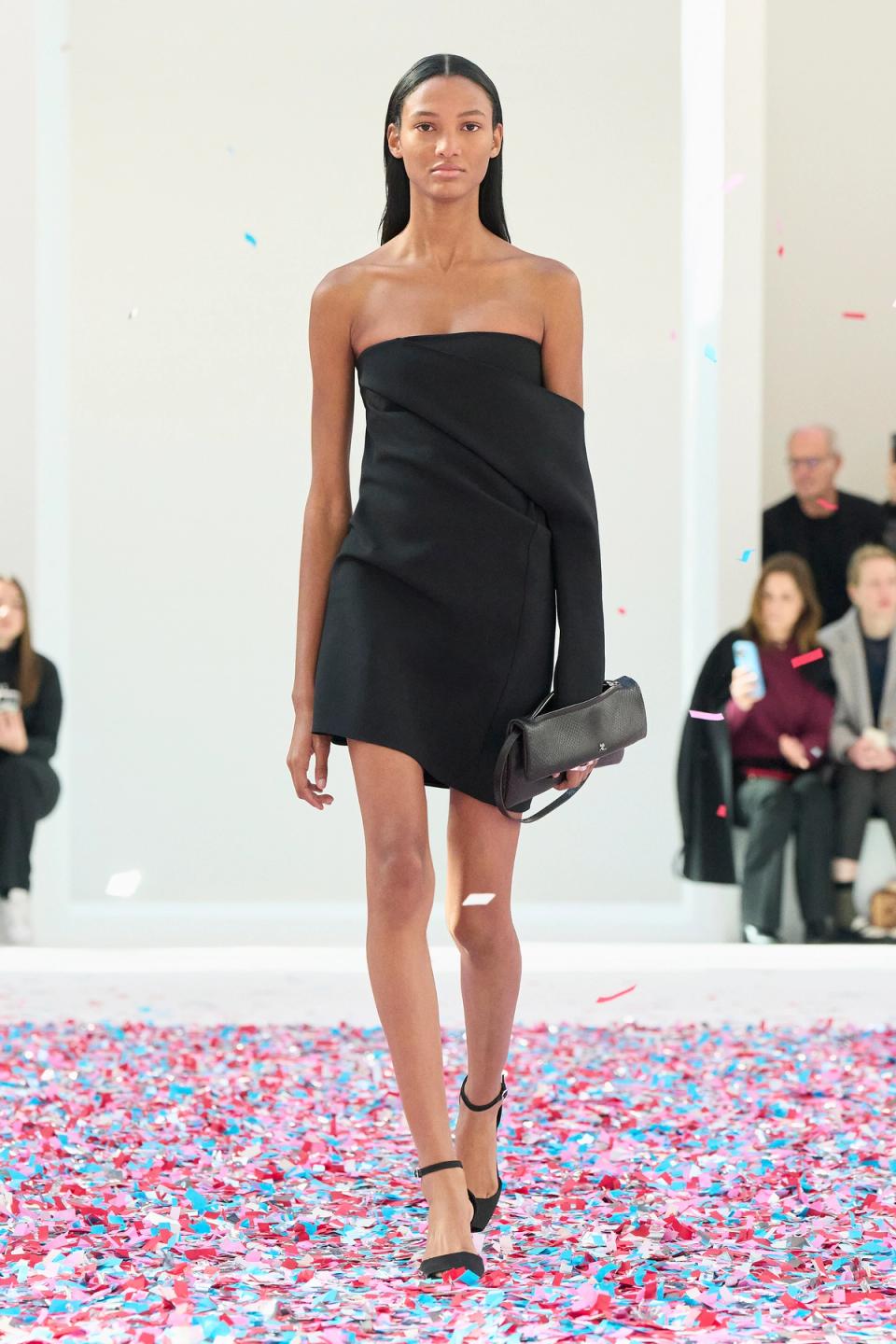 Elegant black strapless dress by Courrèges showcased at a fashion runway with colorful confetti.