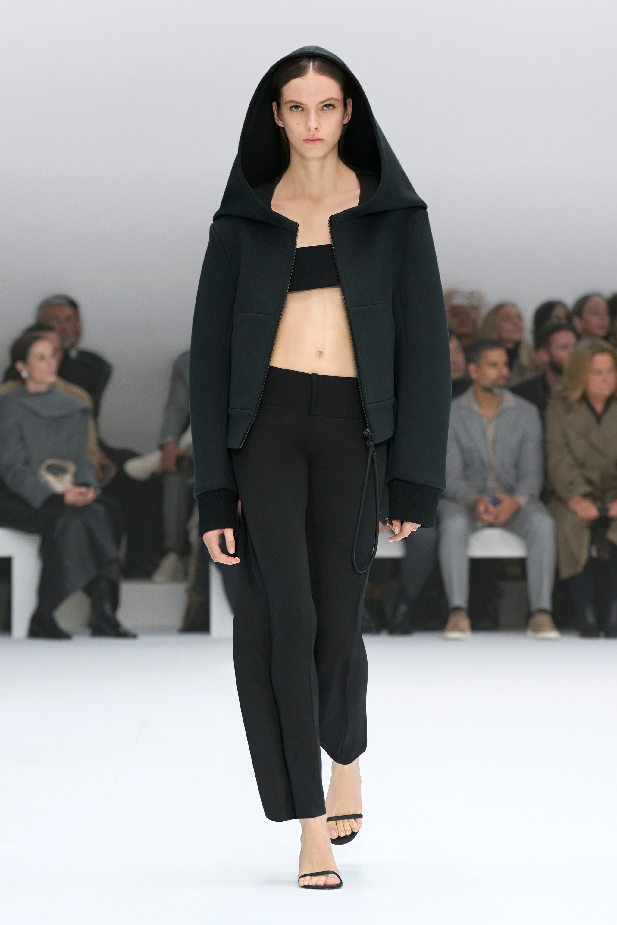 Elegant model in black Courrèges hoodie and pants on runway at a fashion show.