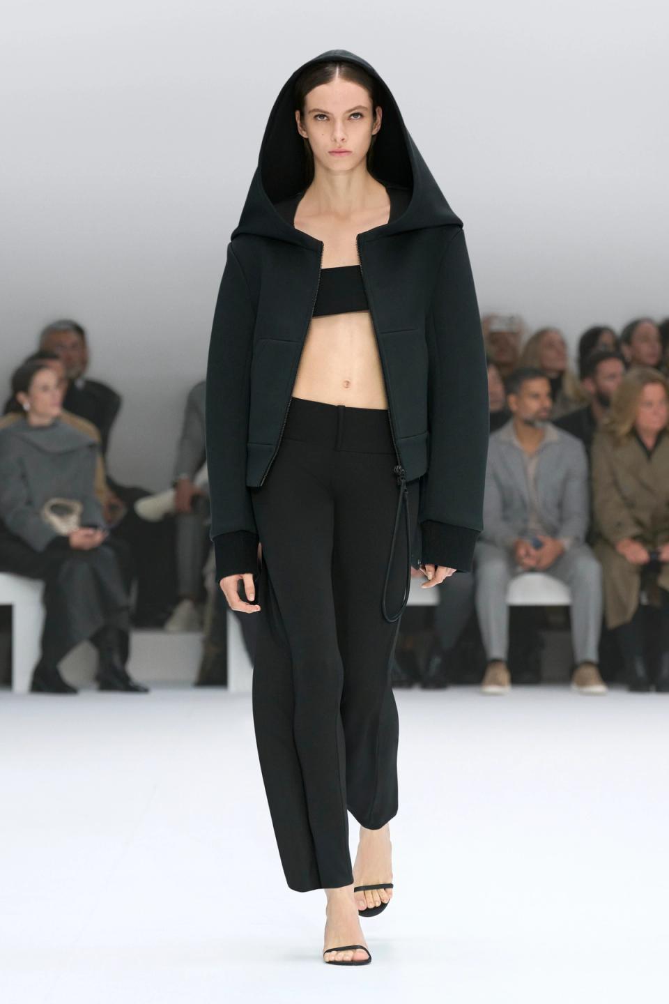 Elegant model in black Courrèges hoodie and pants on runway at a fashion show.