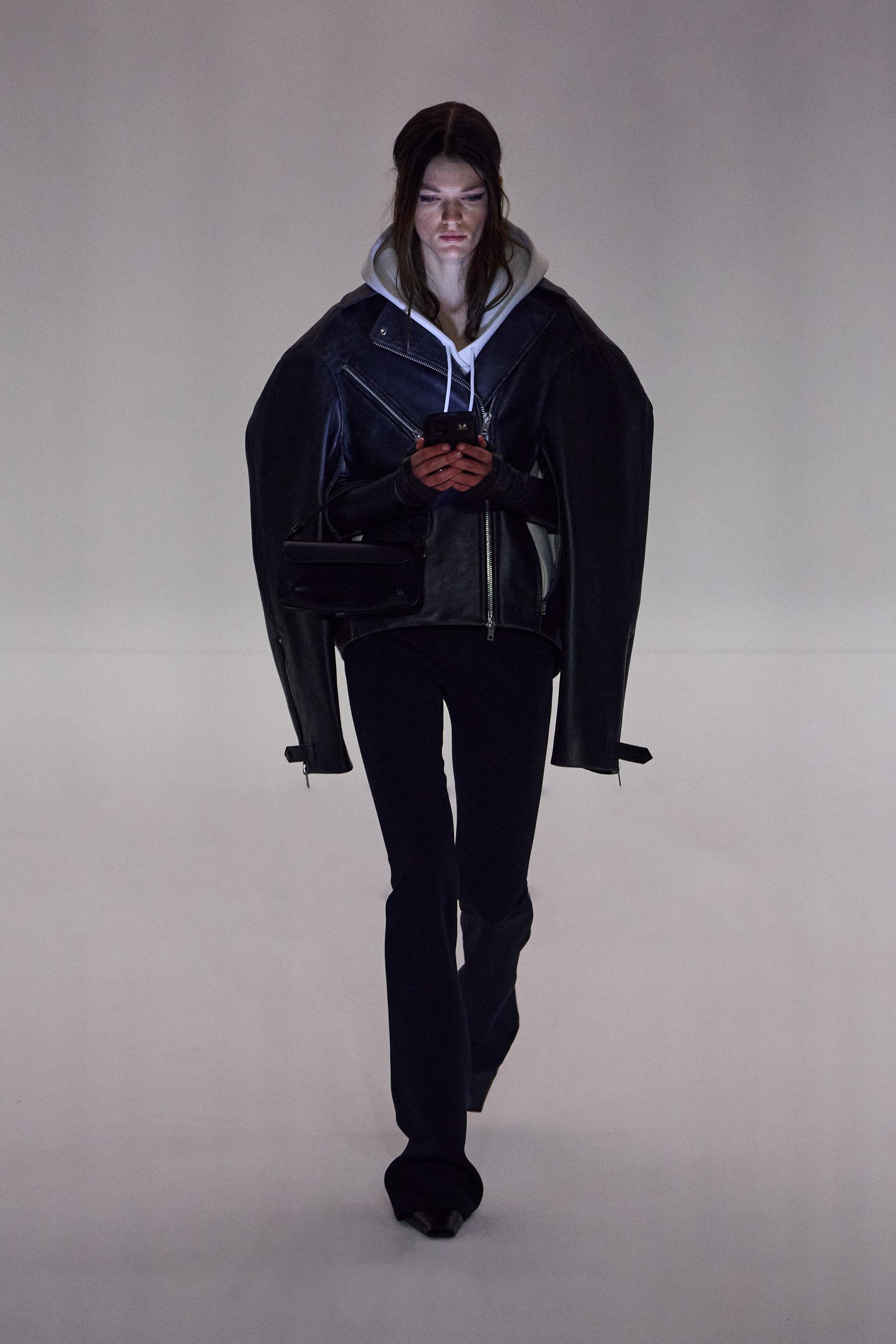 Elegant female model in Courrèges black leather jacket and modern casual style on runway.