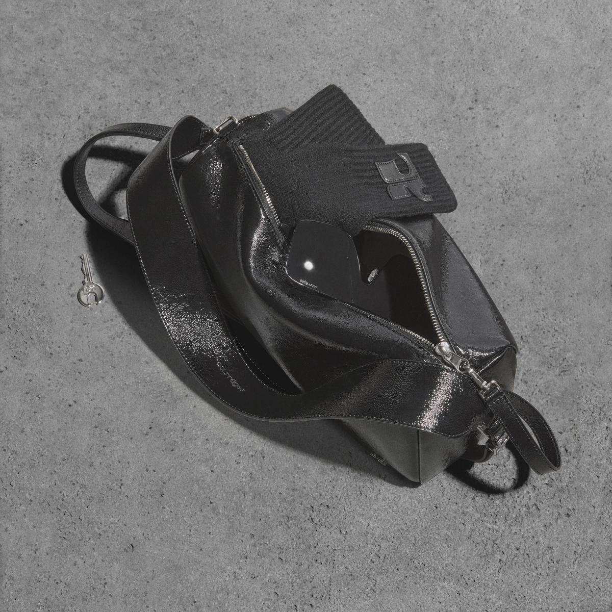 Elegant black Courrèges handbag and accessories on a concrete surface for luxury fashion.