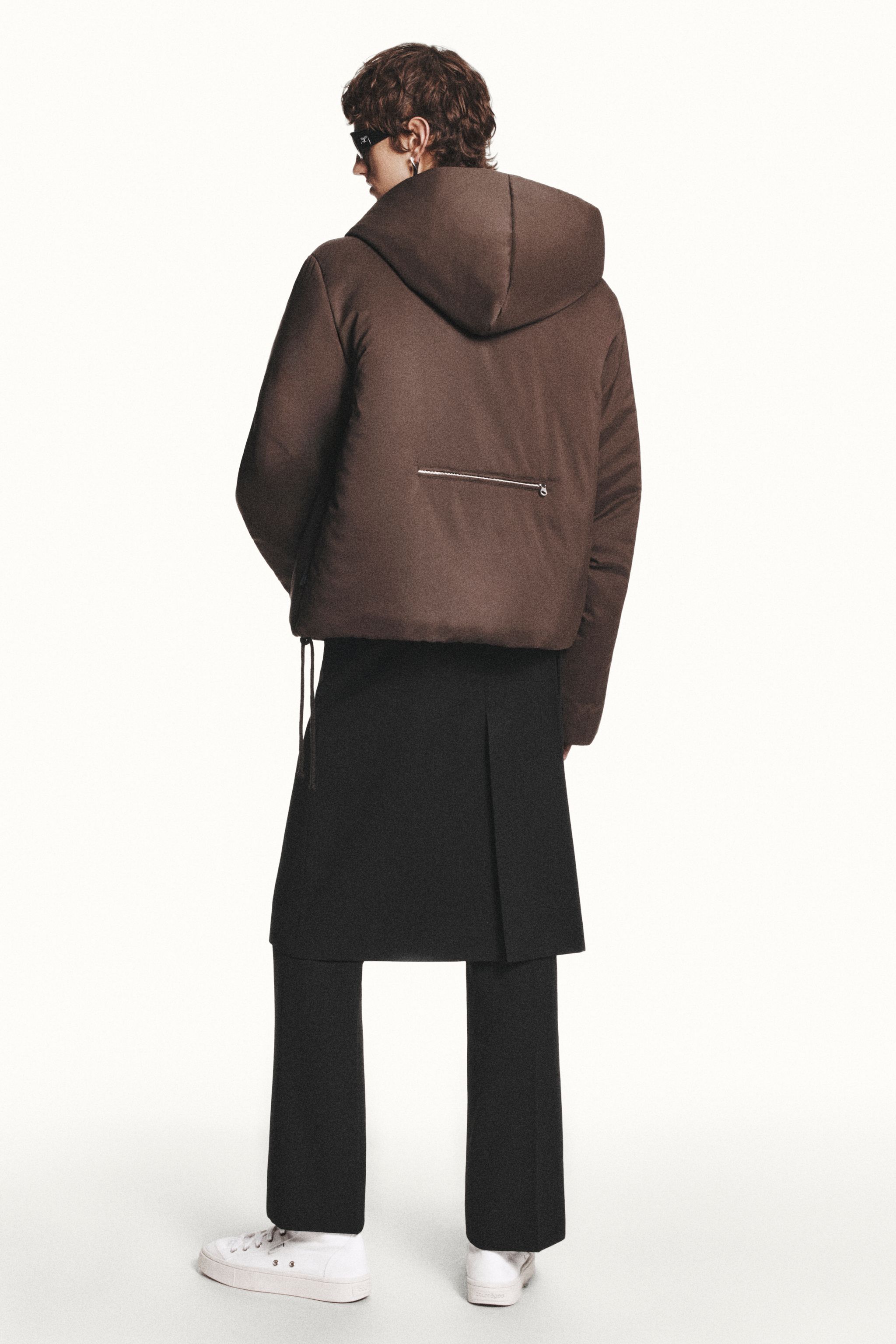 Elegant Courrèges fashion featuring a brown hooded puffer jacket and black trousers.