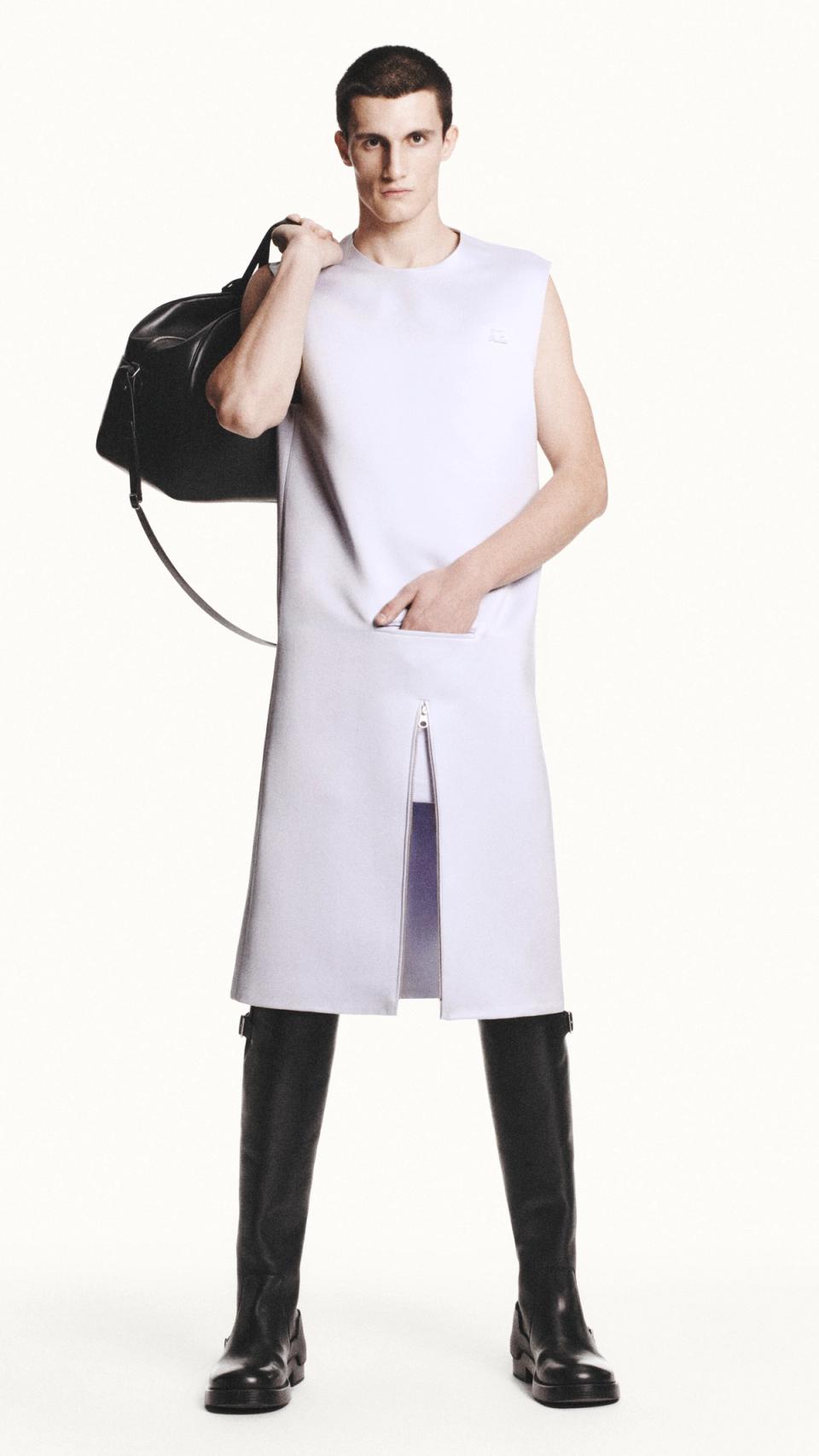 Fashion model in white sleeveless dress with a zip pocket, carrying a black bag, representing Courrèges.