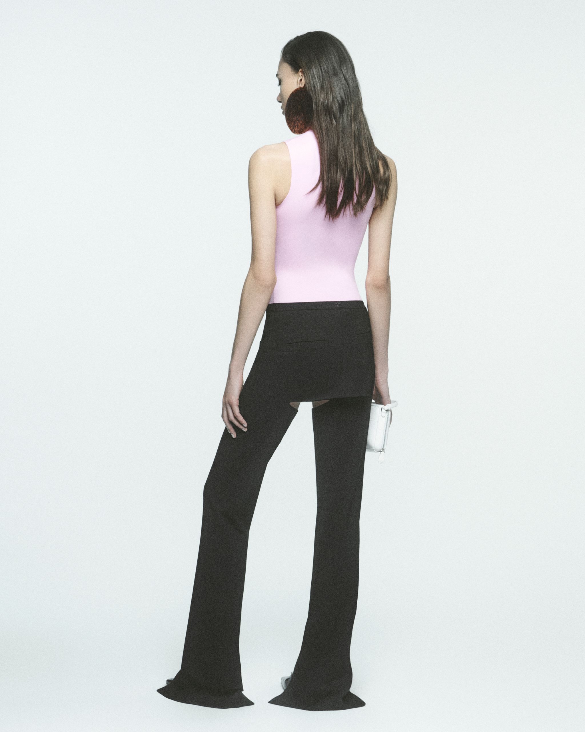 Femme élégante en haut rose et pantalons noirs, présentant la mode Courrèges sur un site e-commerce.