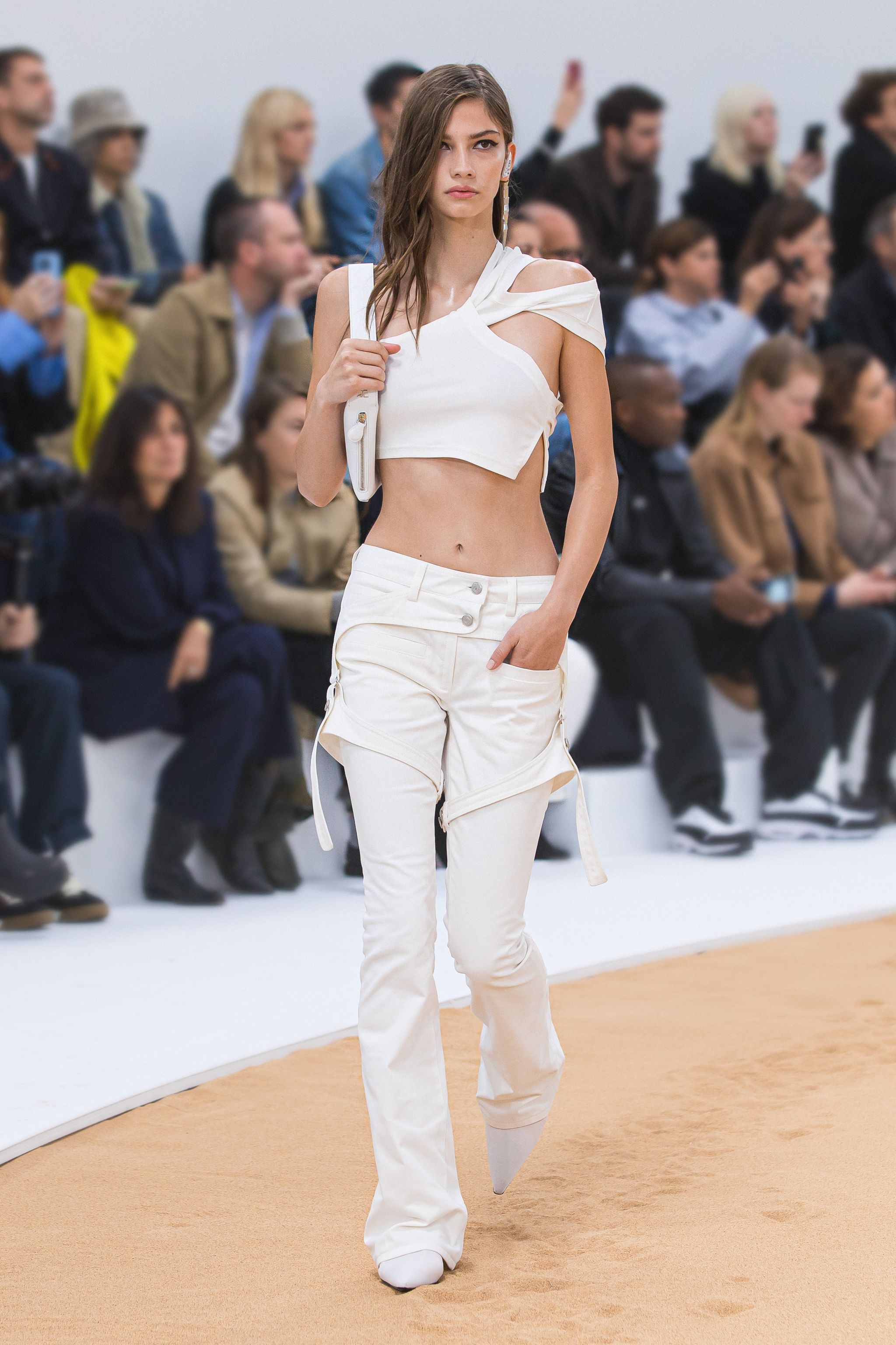 Elegant young woman in off-shoulder white top and cargo pants at Courrèges fashion show.