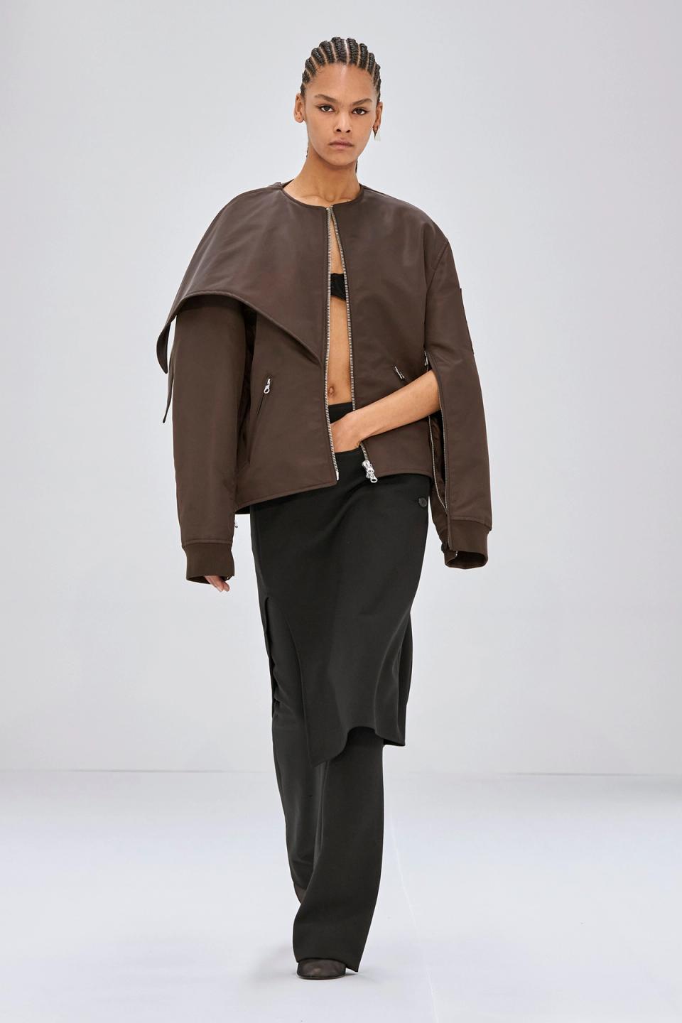Elegant model wearing Courrèges stylish brown jacket and black trousers on a minimal background.