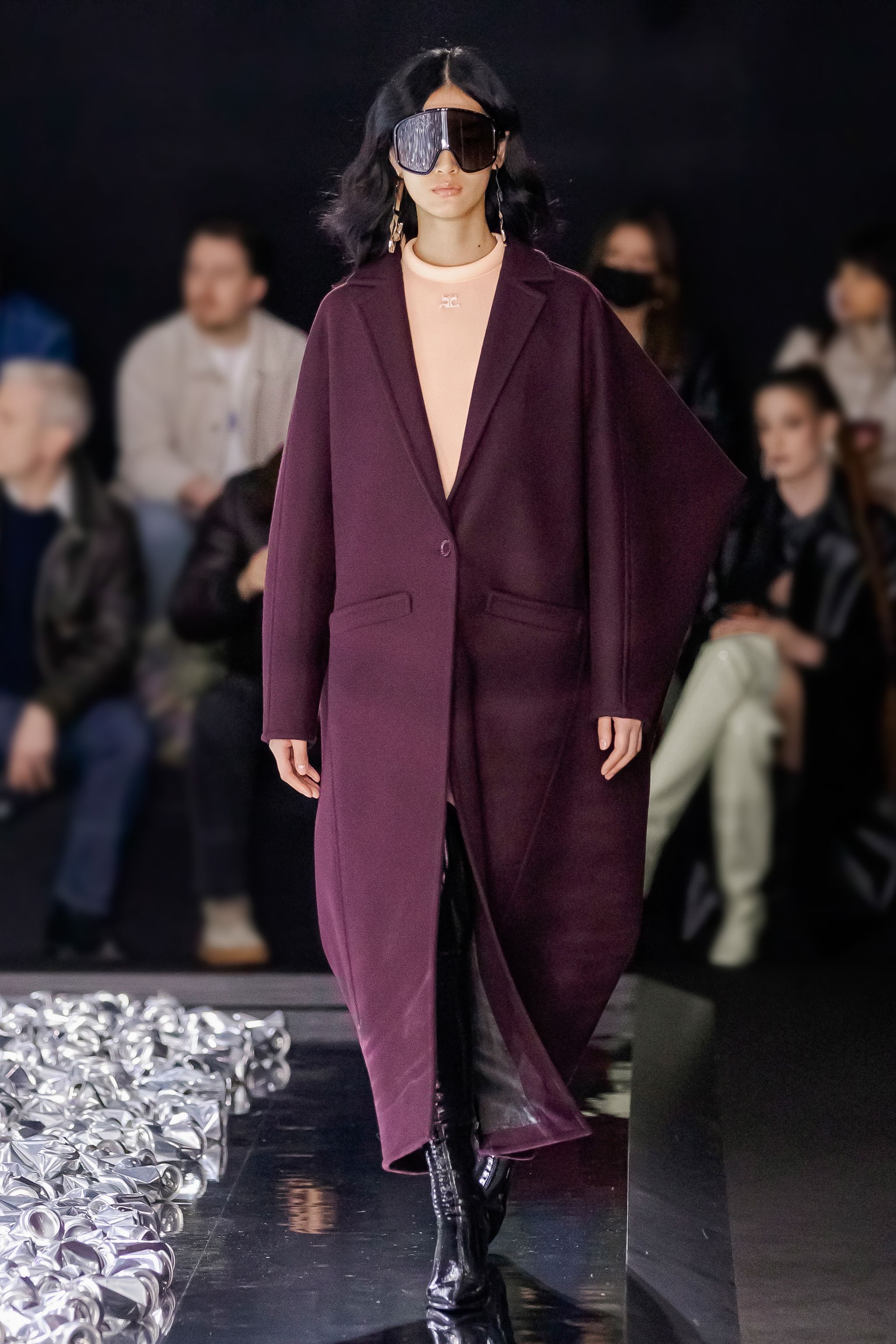 Elegant Courrèges fashion model wearing a purple coat on runway with audience in background.