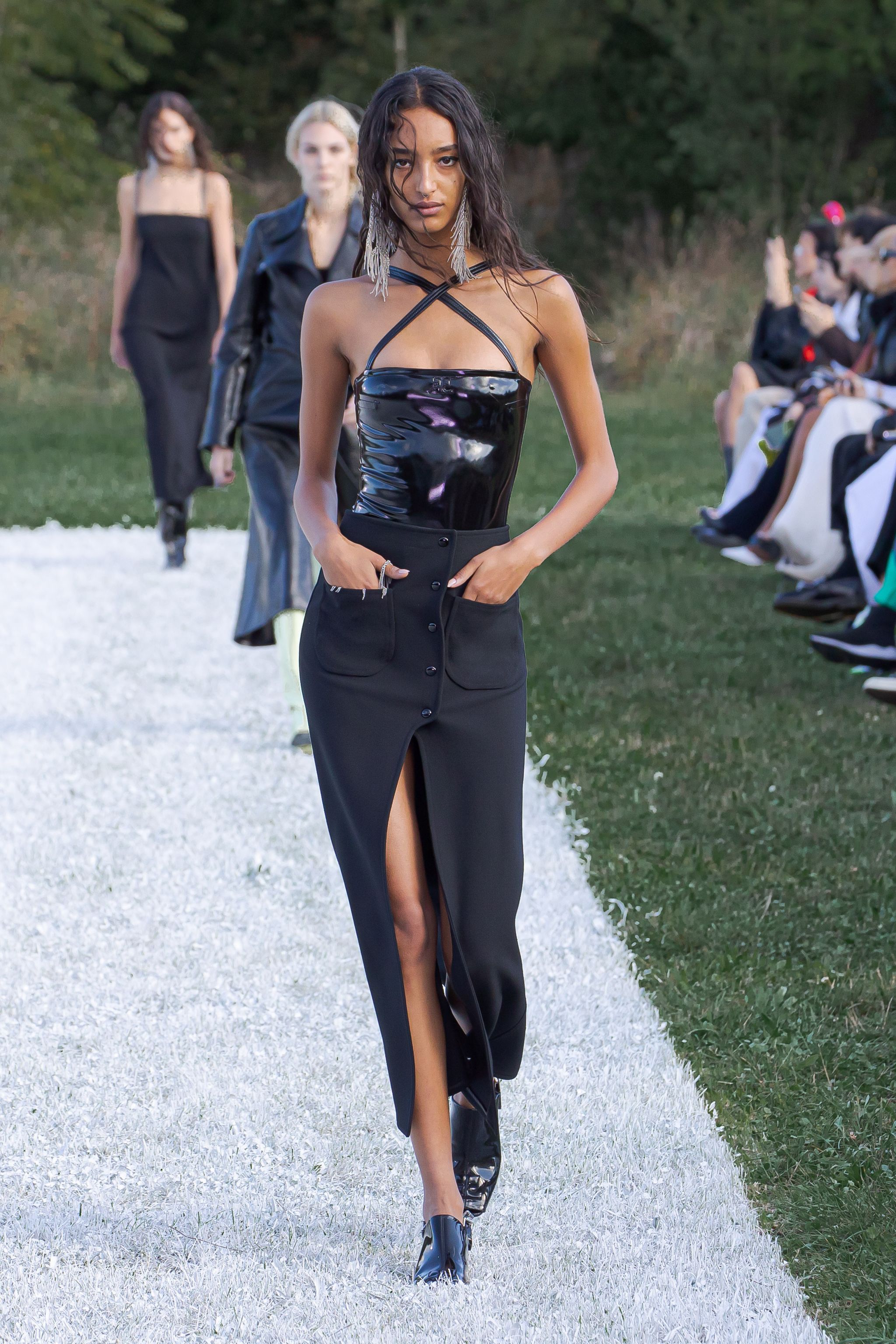 Elegant model wearing a black patent leather top and a long slit skirt on the fashion runway.