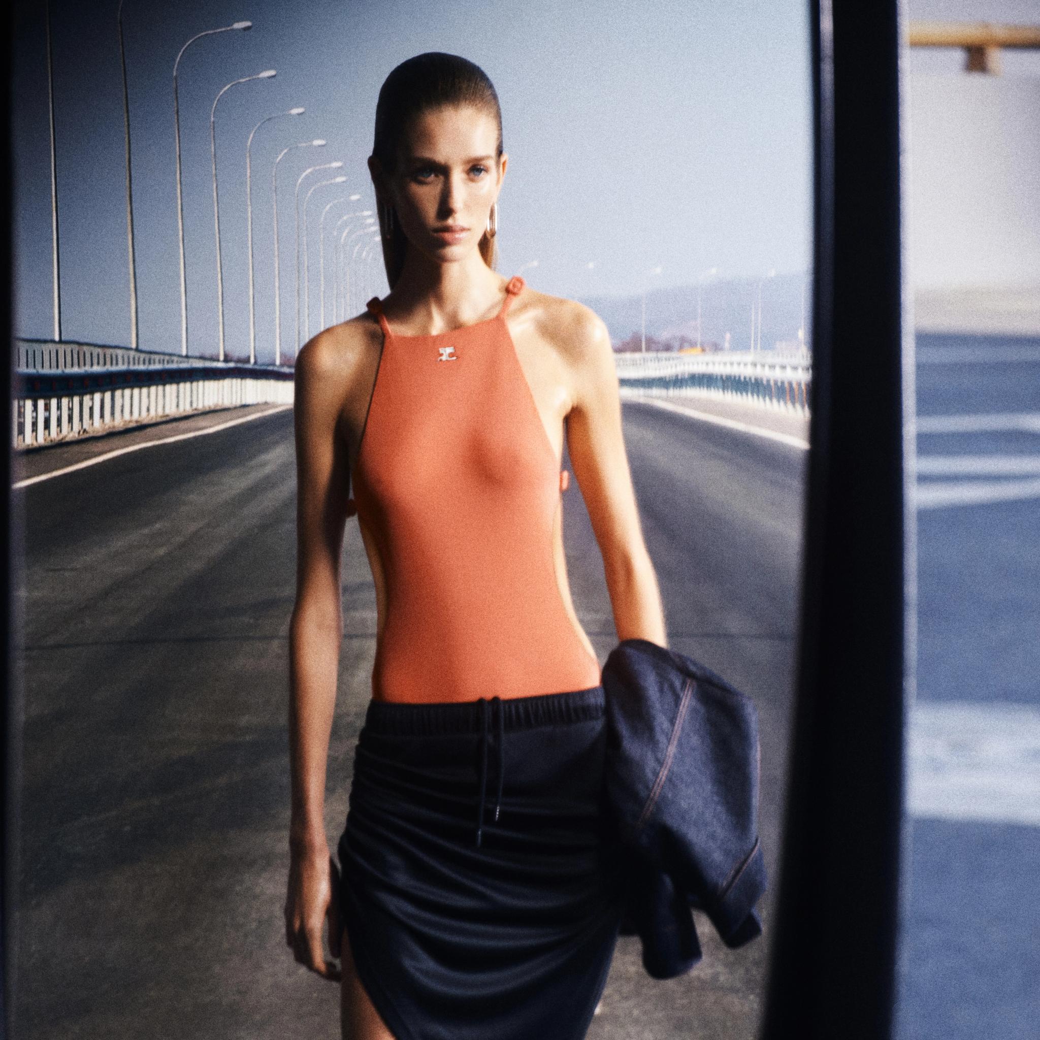 Top sans manches orange élégant de Courrèges porté par un mannequin sur un pont urbain, parfait pour la mode moderne.